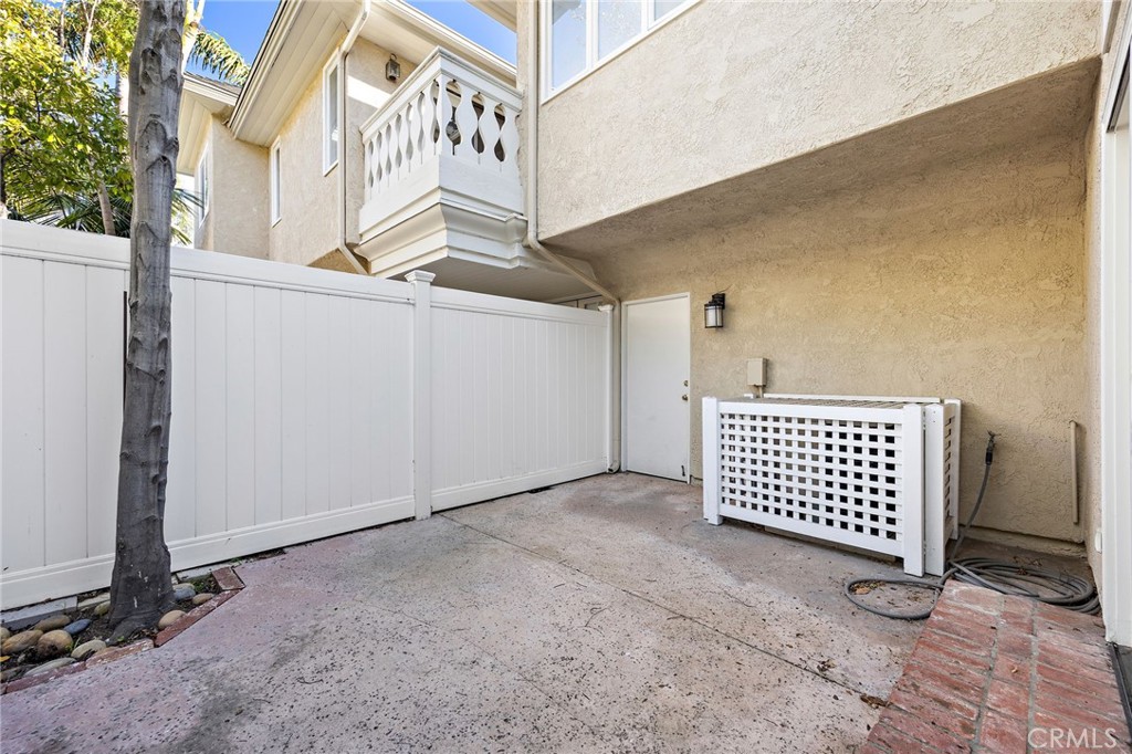 Concrete patio enclosed by a white privacy fence, with a small balcony and lattice-covered equipment screen.