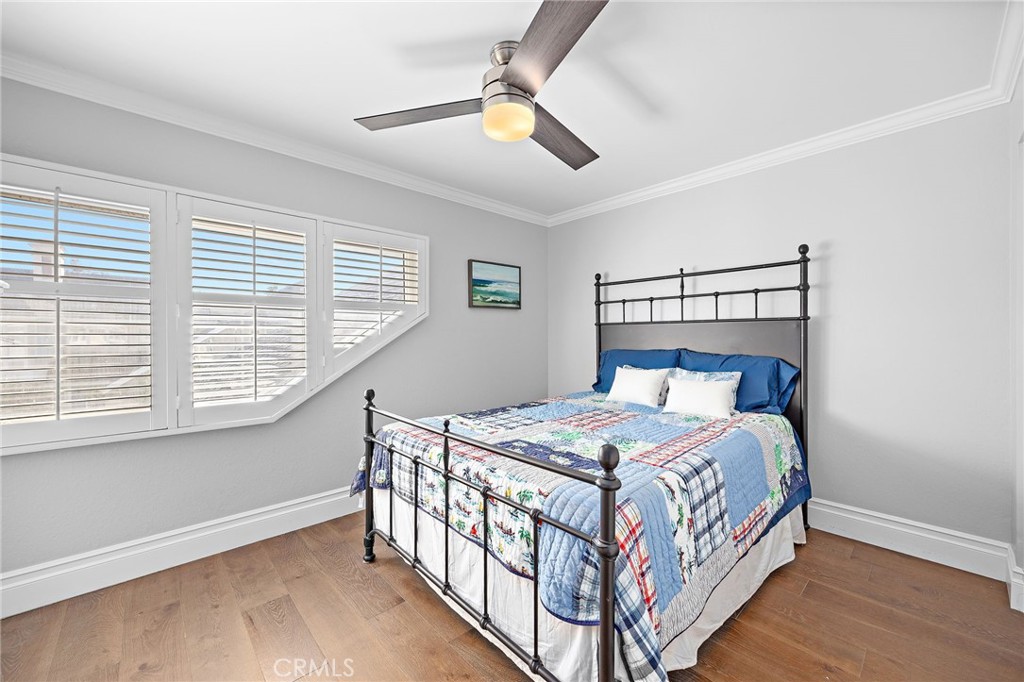 Bedroom with a patchwork quilt, black metal bed, and angled windows with plantation shutters.