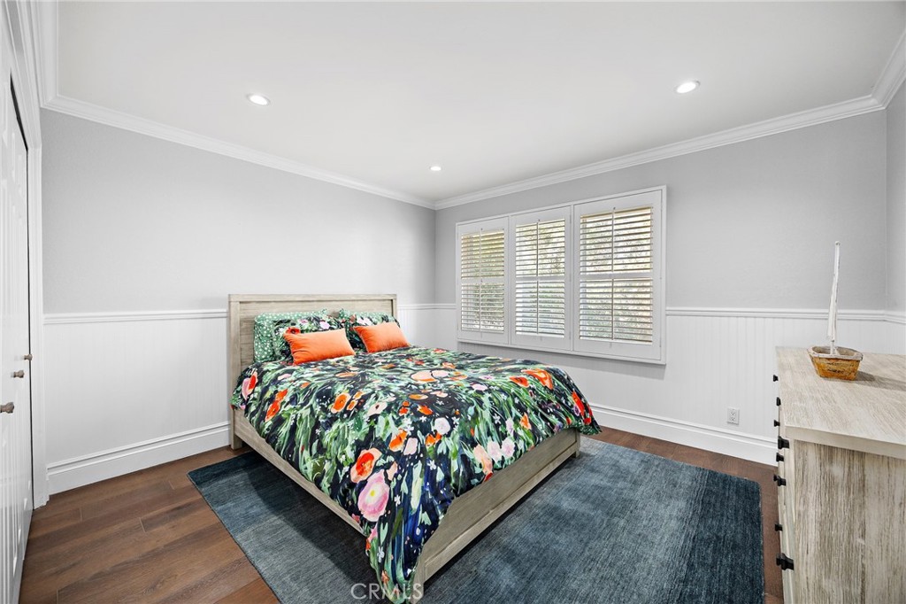 Bedroom with colorful floral bedding, plantation shutters, and a blue-gray rug.