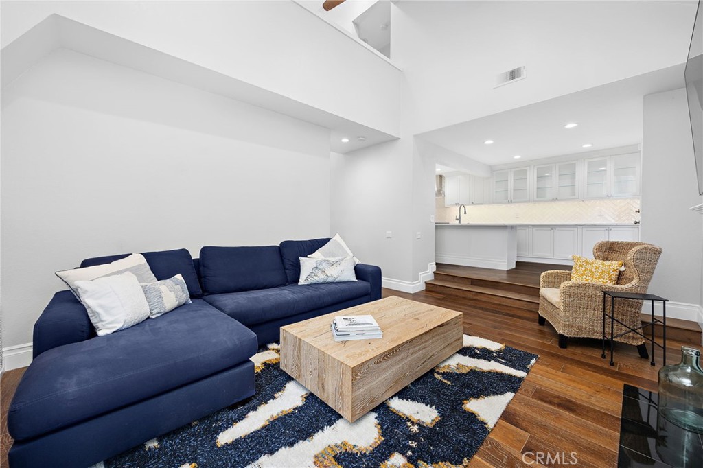 Living room with a navy sectional, patterned rug, and steps up to a bright white kitchen.