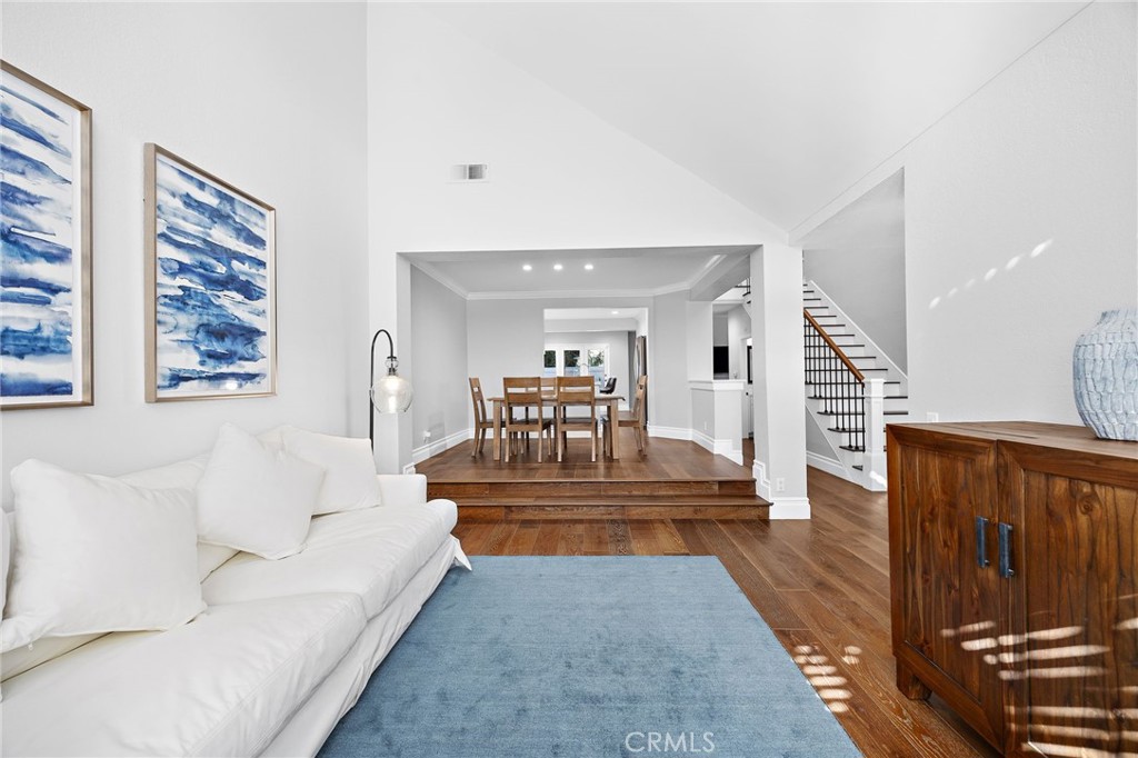 Living room with a white sofa and blue rug opening to a raised dining area and staircase.