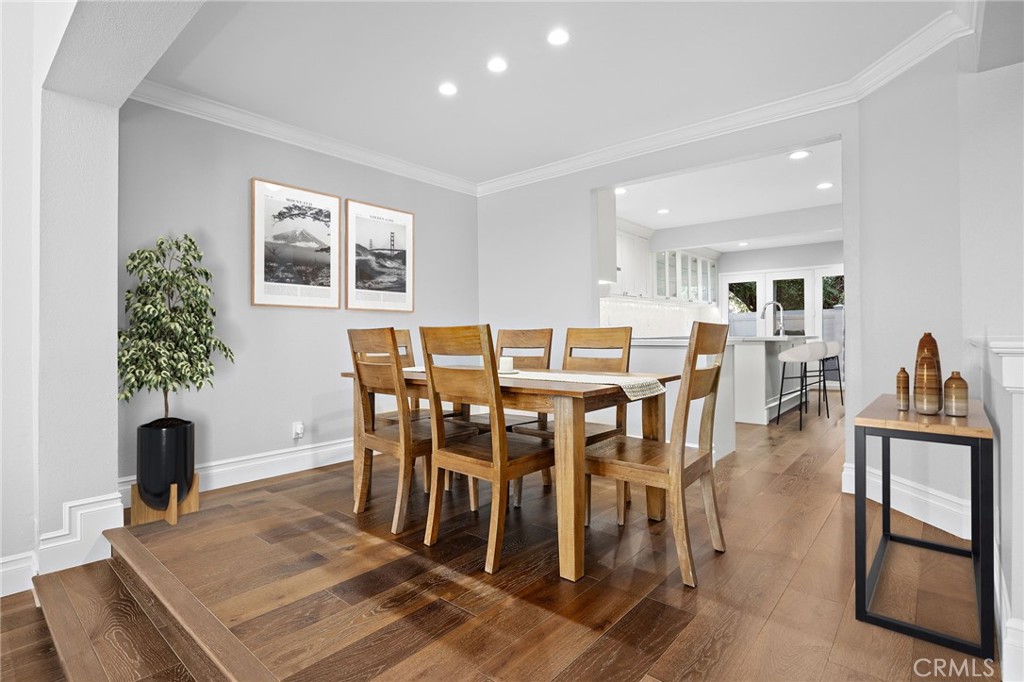 Dining room with a wooden table and chairs, hardwood floors, and an open view into the kitchen.