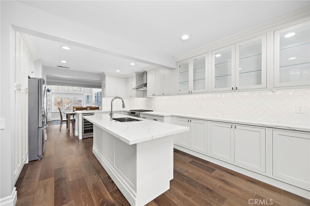 Bright white kitchen with a marble-veined island, glass-front cabinets, and dark wood floors.