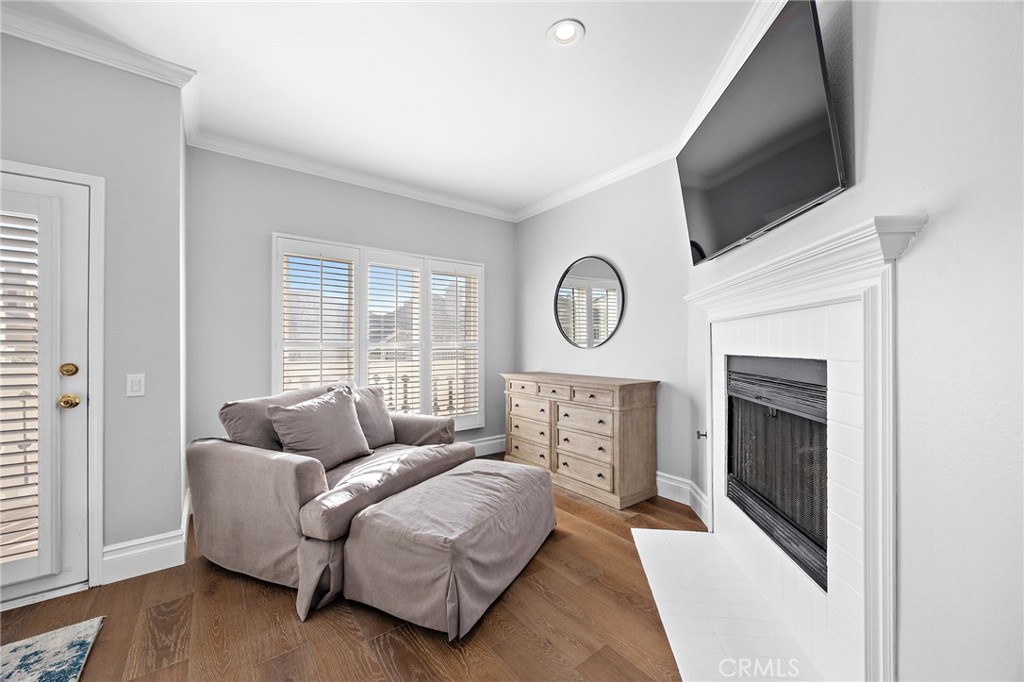 Living room with a chaise sofa, shuttered windows, and a white fireplace beneath a wall-mounted TV.