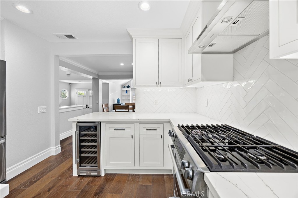 White kitchen with herringbone tile backsplash, stainless gas range, and built-in wine refrigerator.
