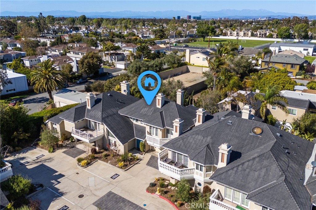 Aerial view of attached homes with balconies, a paved parking area, and distant mountains.
