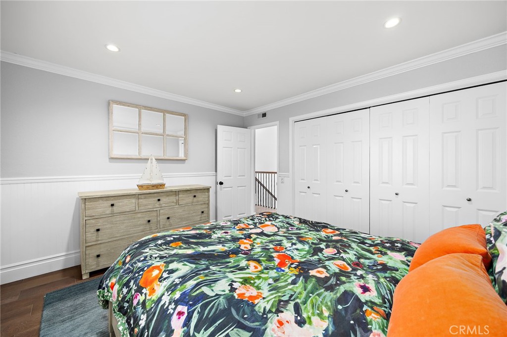 Bedroom with floral bedding, orange pillows, a wood dresser, and white paneled closet doors.