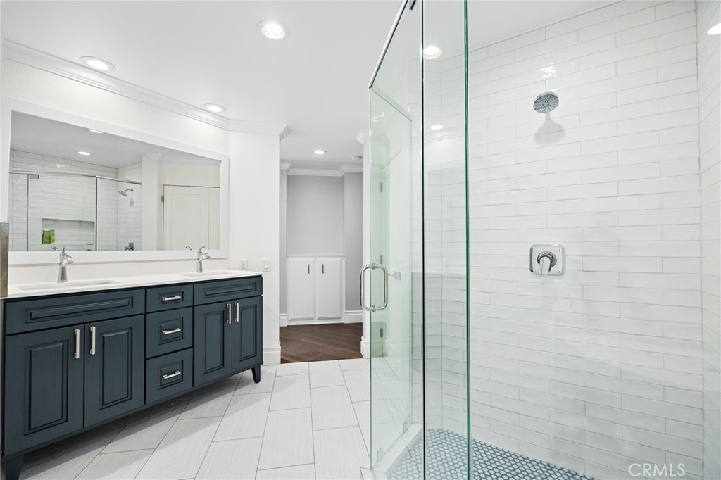Bathroom with a dark blue double vanity and glass-enclosed white-tile shower.