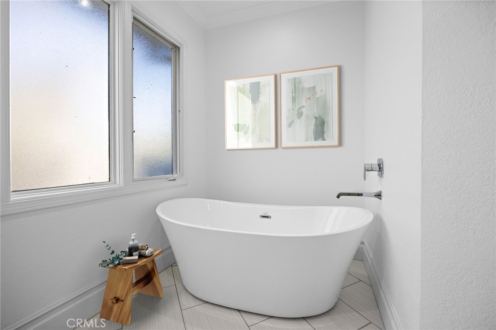 White freestanding soaking tub beneath frosted windows in a bright bathroom.