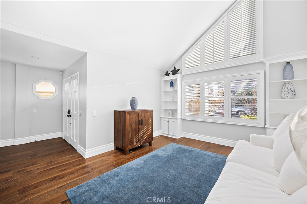 Living room with vaulted ceiling, tall shuttered windows, white sofa, and blue rug.