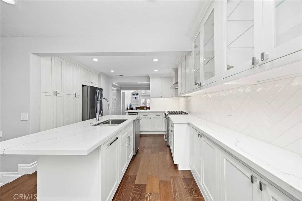Bright white kitchen with a large quartz island, herringbone backsplash, and warm wood flooring.