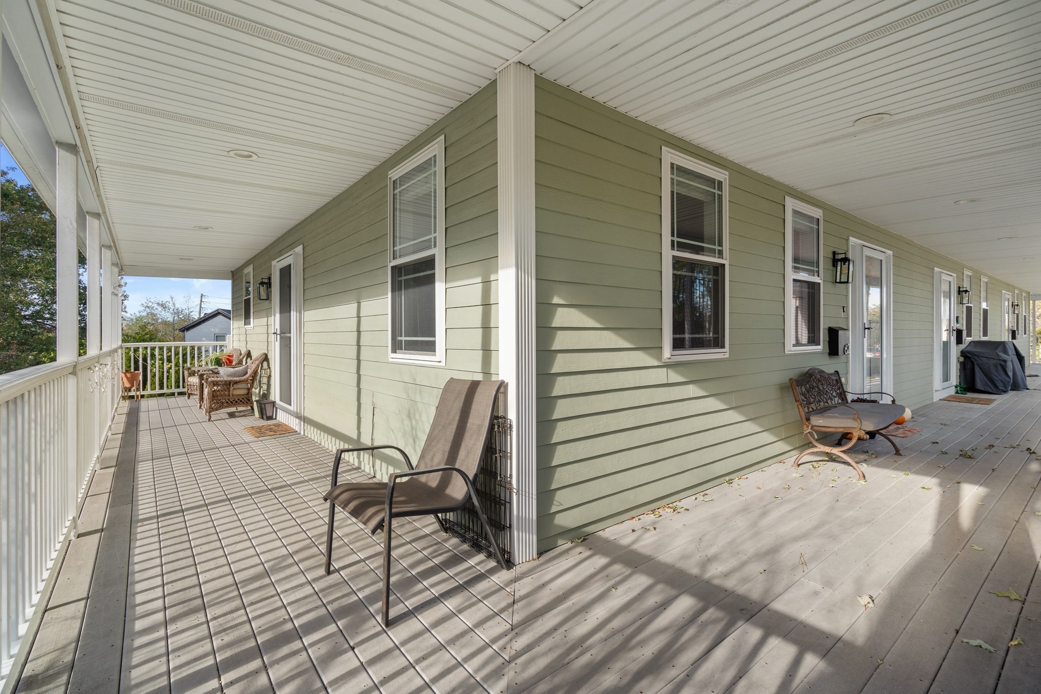 Covered porch with sage-green siding, white railing, and seating along the house.