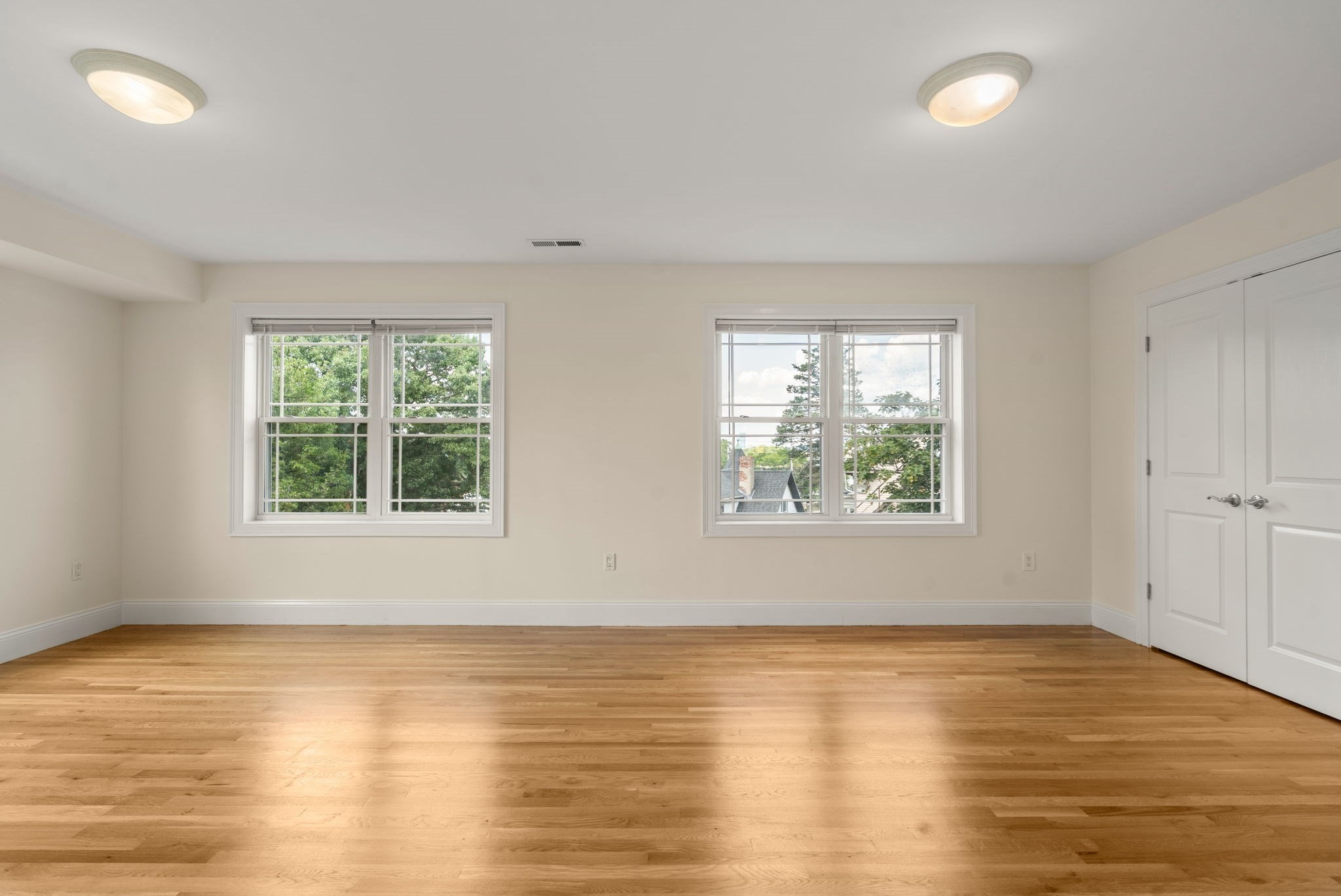 Empty room with two windows, double closet doors, and polished hardwood floors.