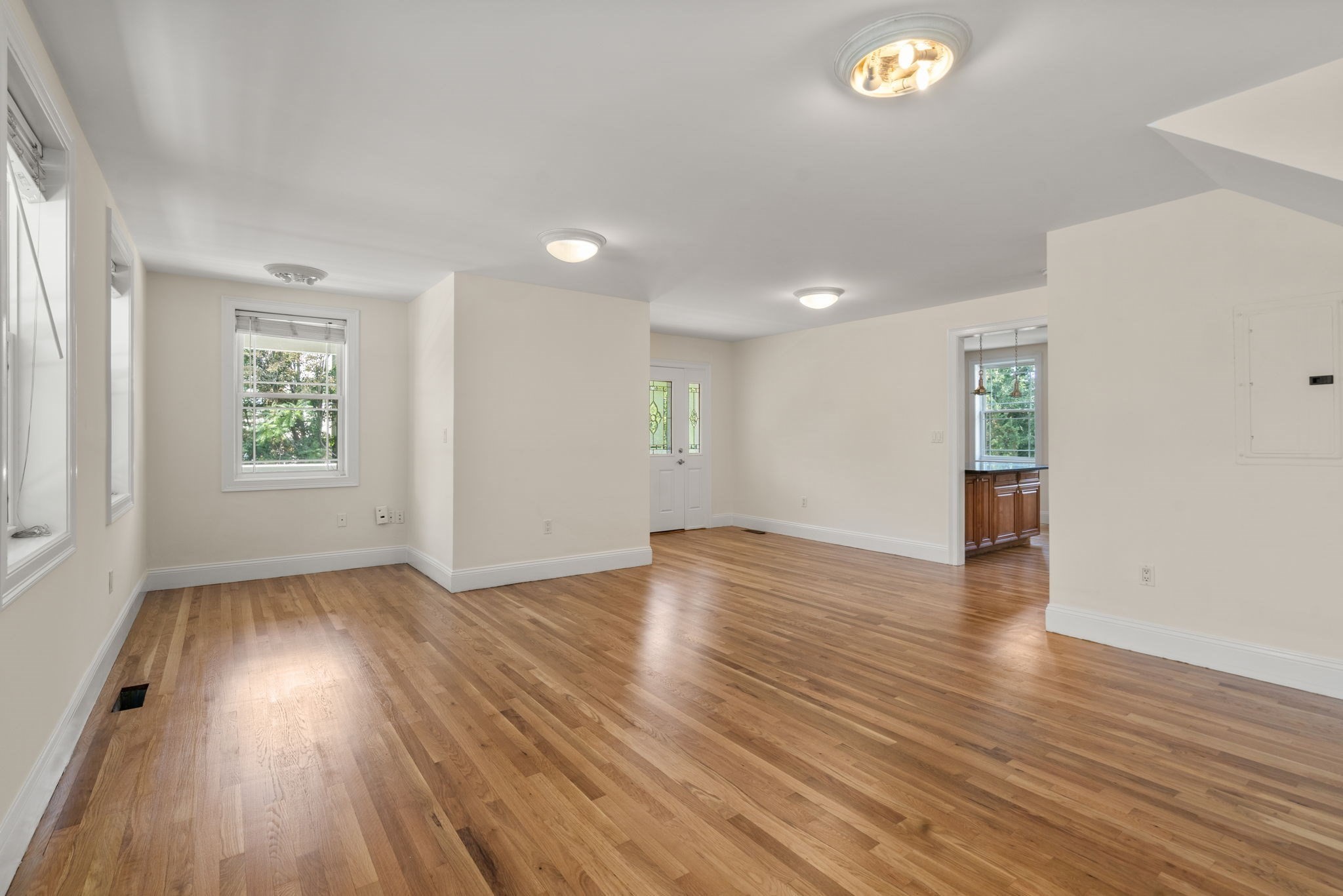 Empty living and dining area with hardwood floors, multiple windows, and a glass-paneled entry door.
