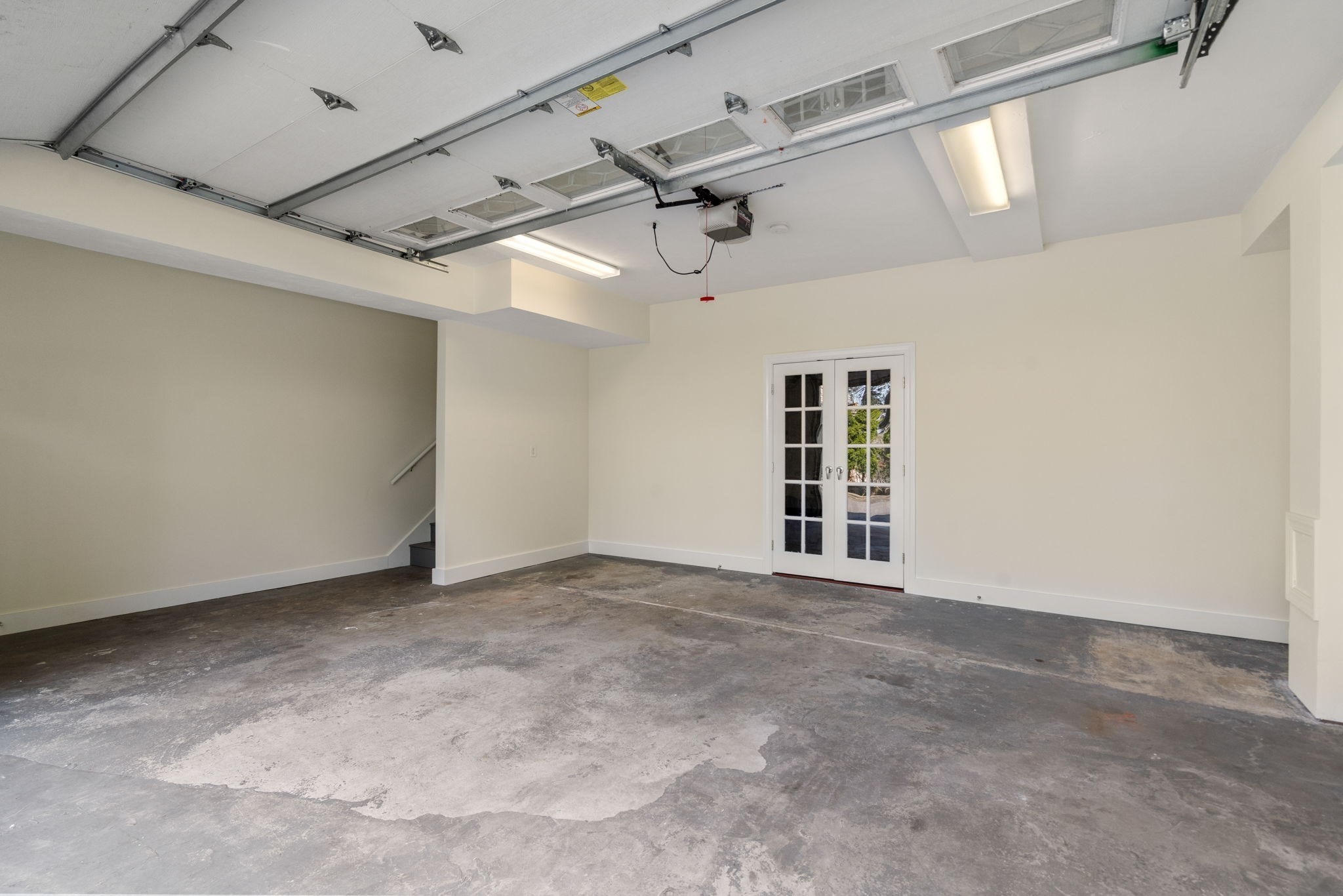 Empty garage with a raised overhead door, worn concrete floor, and French doors.