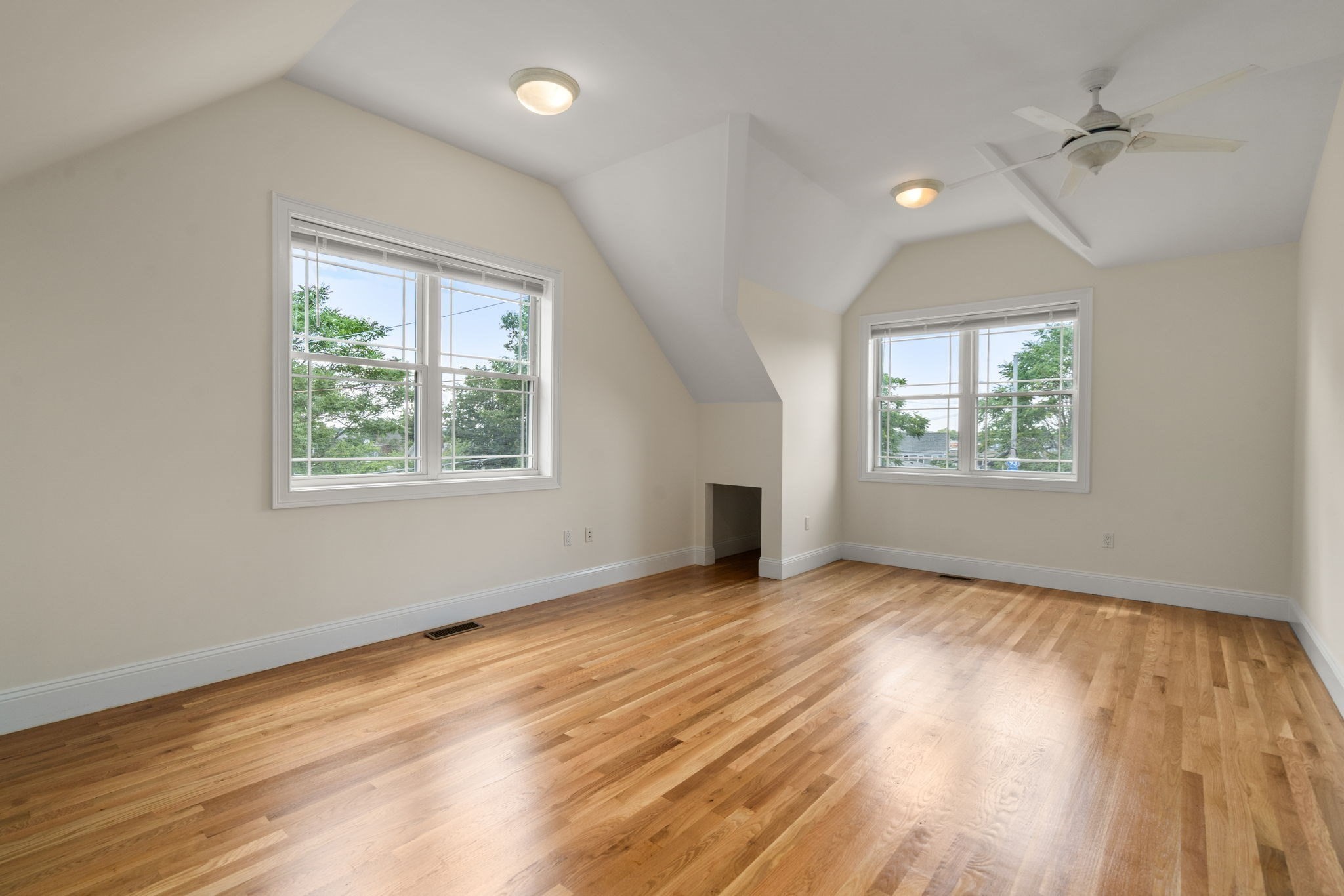 Empty bedroom with vaulted ceiling, hardwood floors, two windows, and a ceiling fan.
