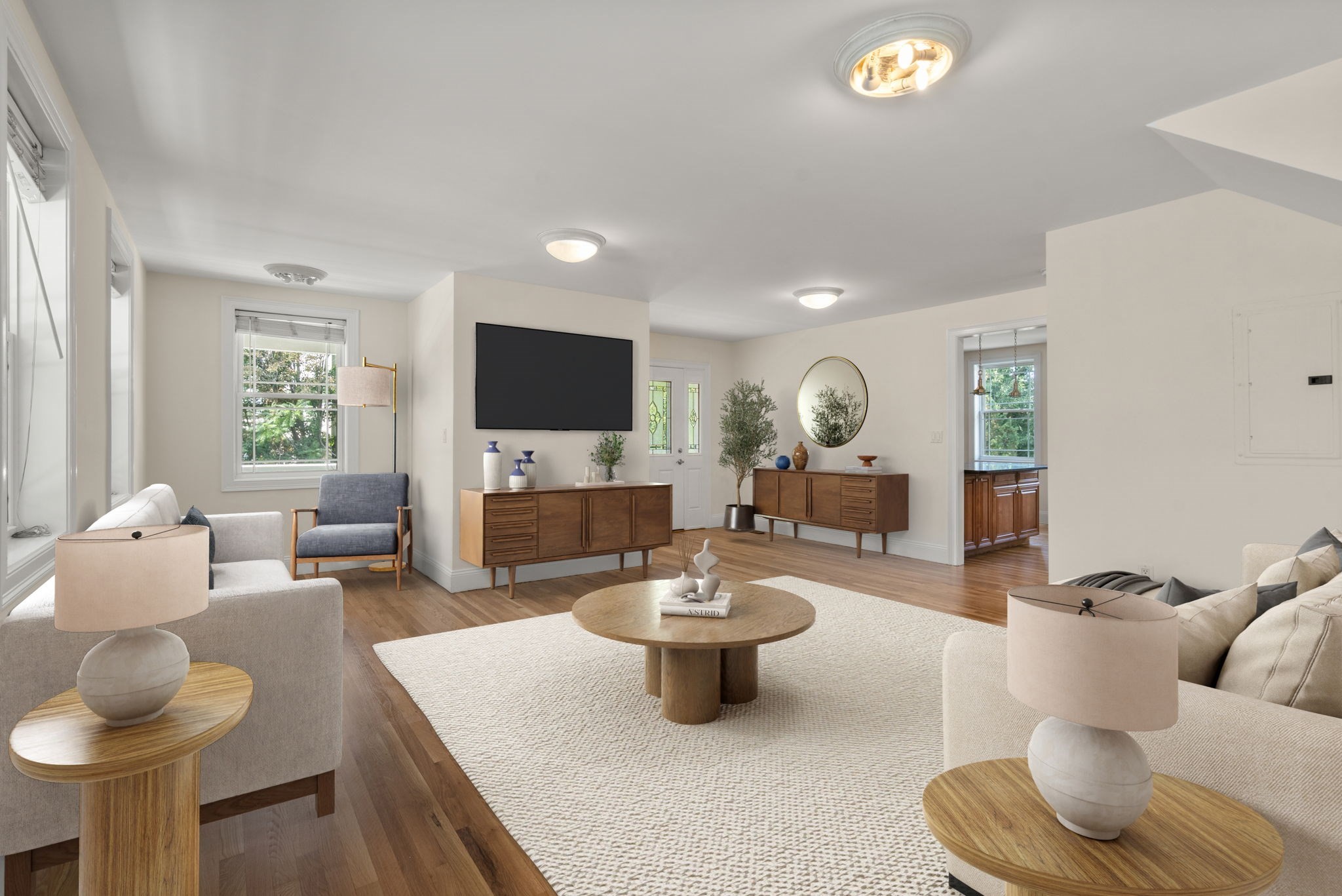 Staged living room with cream sofas, a round wood coffee table, hardwood floors, and a wall-mounted television.