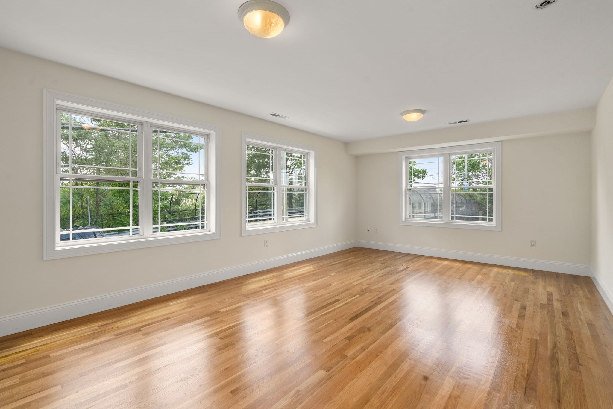 Empty room with polished hardwood floors and several large windows.