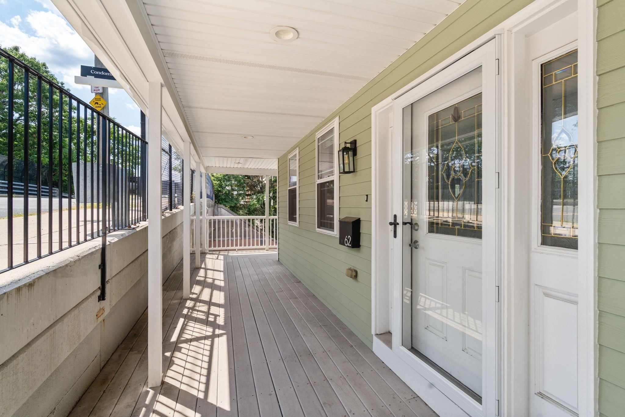 Covered porch with pale green siding, white decorative glass doors, and a black railing.