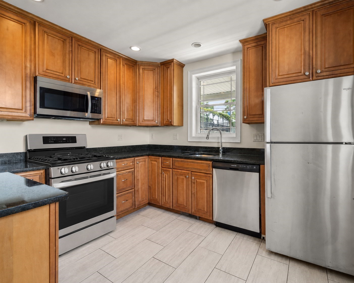 Kitchen with wood cabinets, dark countertops, stainless steel appliances, and a window above the sink.