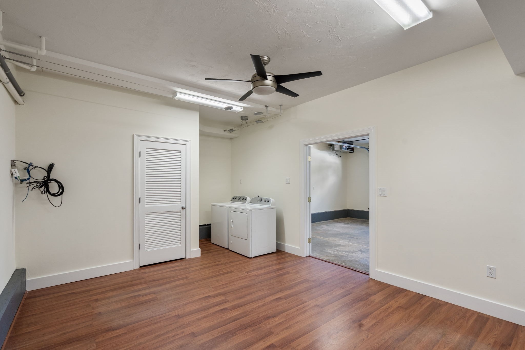 Laundry room with a washer and dryer, wood-look flooring, and a doorway to an adjoining concrete-floored room.