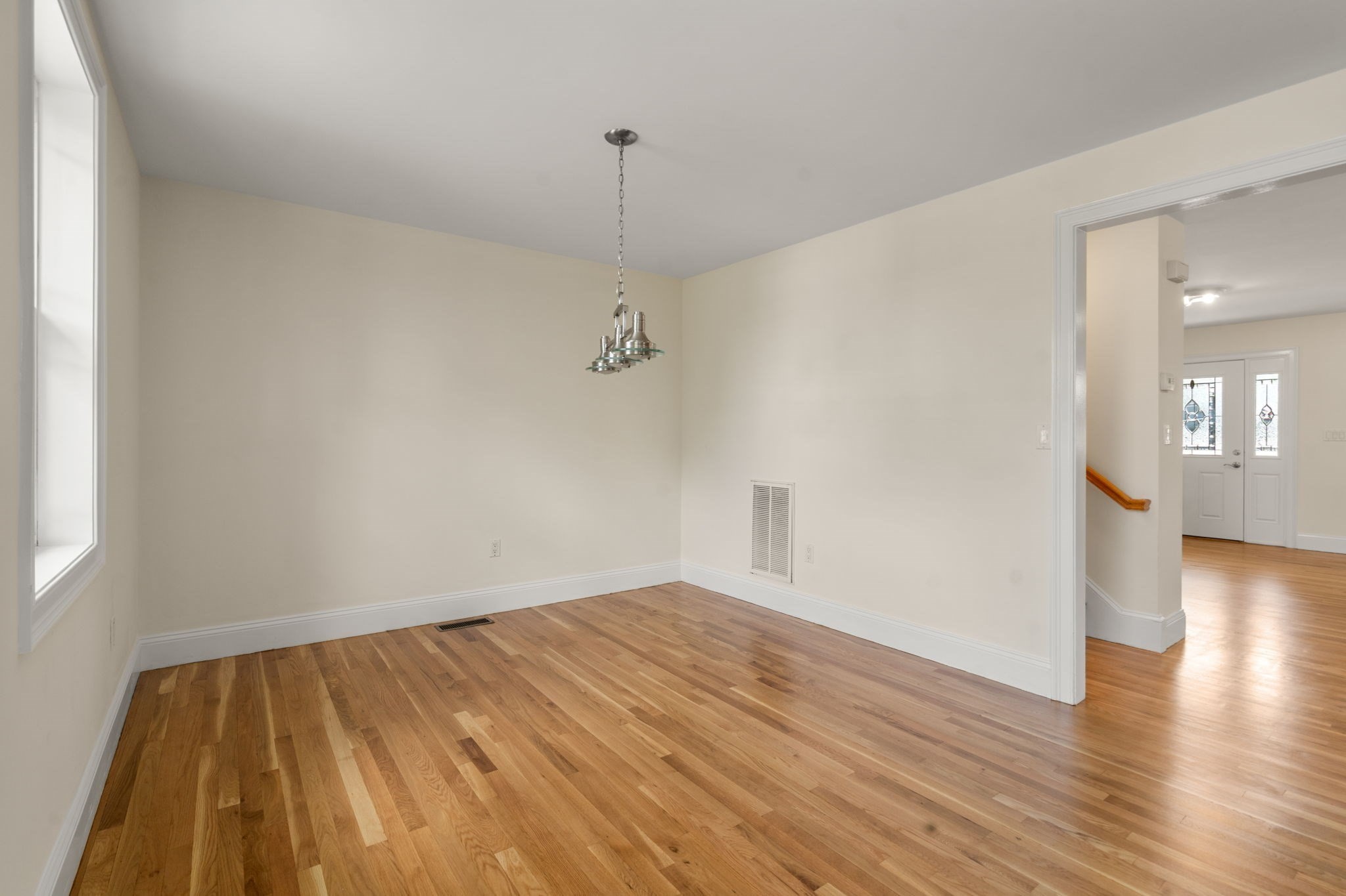 Vacant dining room with hardwood floors, pendant light, and a view through to the entry hall.