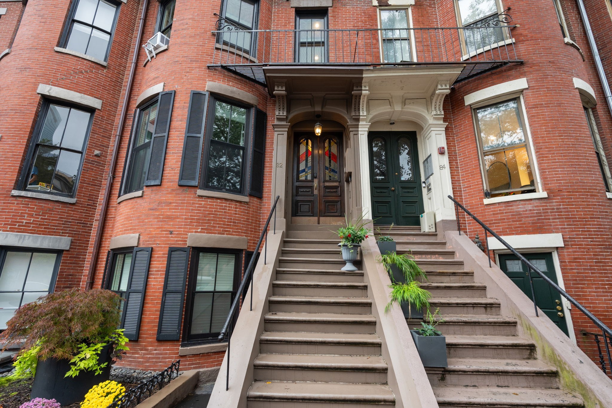 Red-brick townhouse entrance with twin brownstone staircases, ornate doorways, and potted plants.