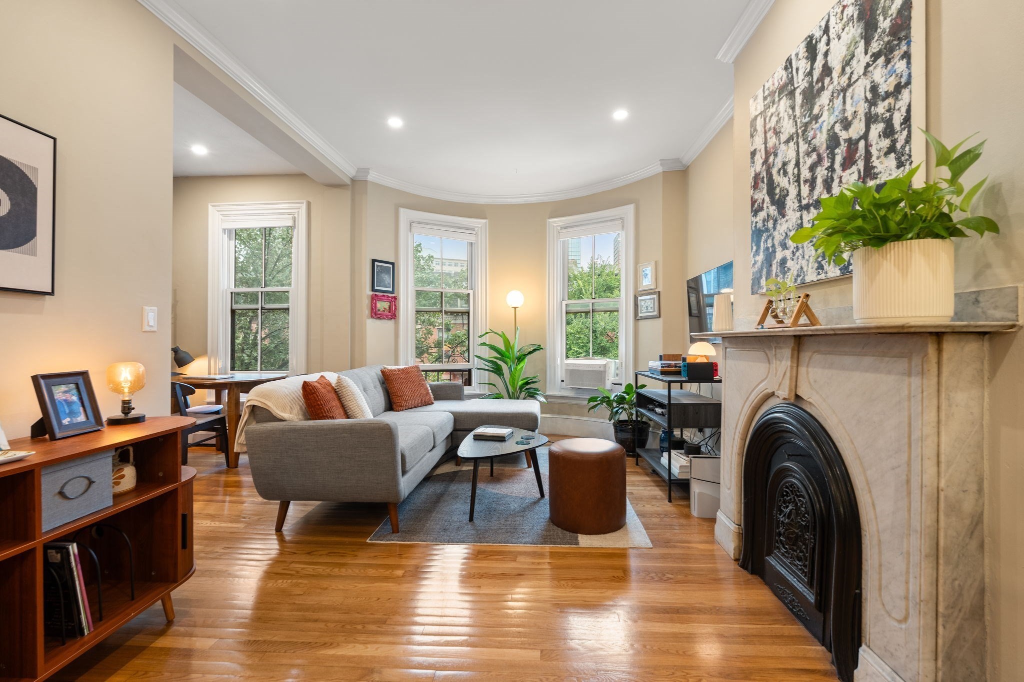 Living room with a curved bay of tall windows, hardwood floors, and a marble fireplace.
