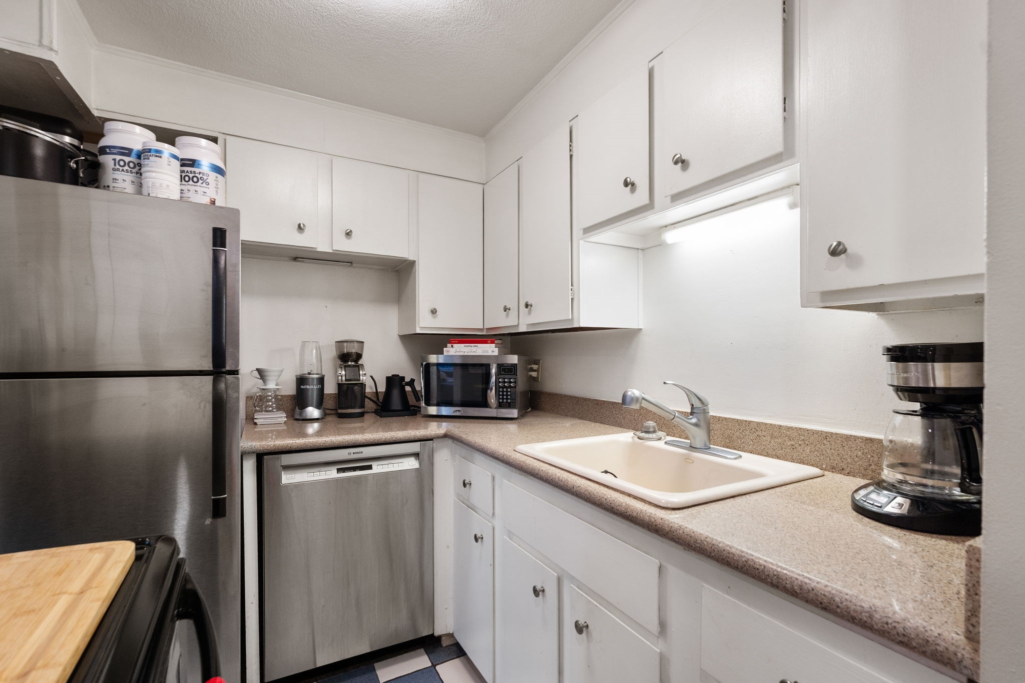 Compact kitchen with white cabinets, speckled counters, stainless appliances, and a double-basin sink.