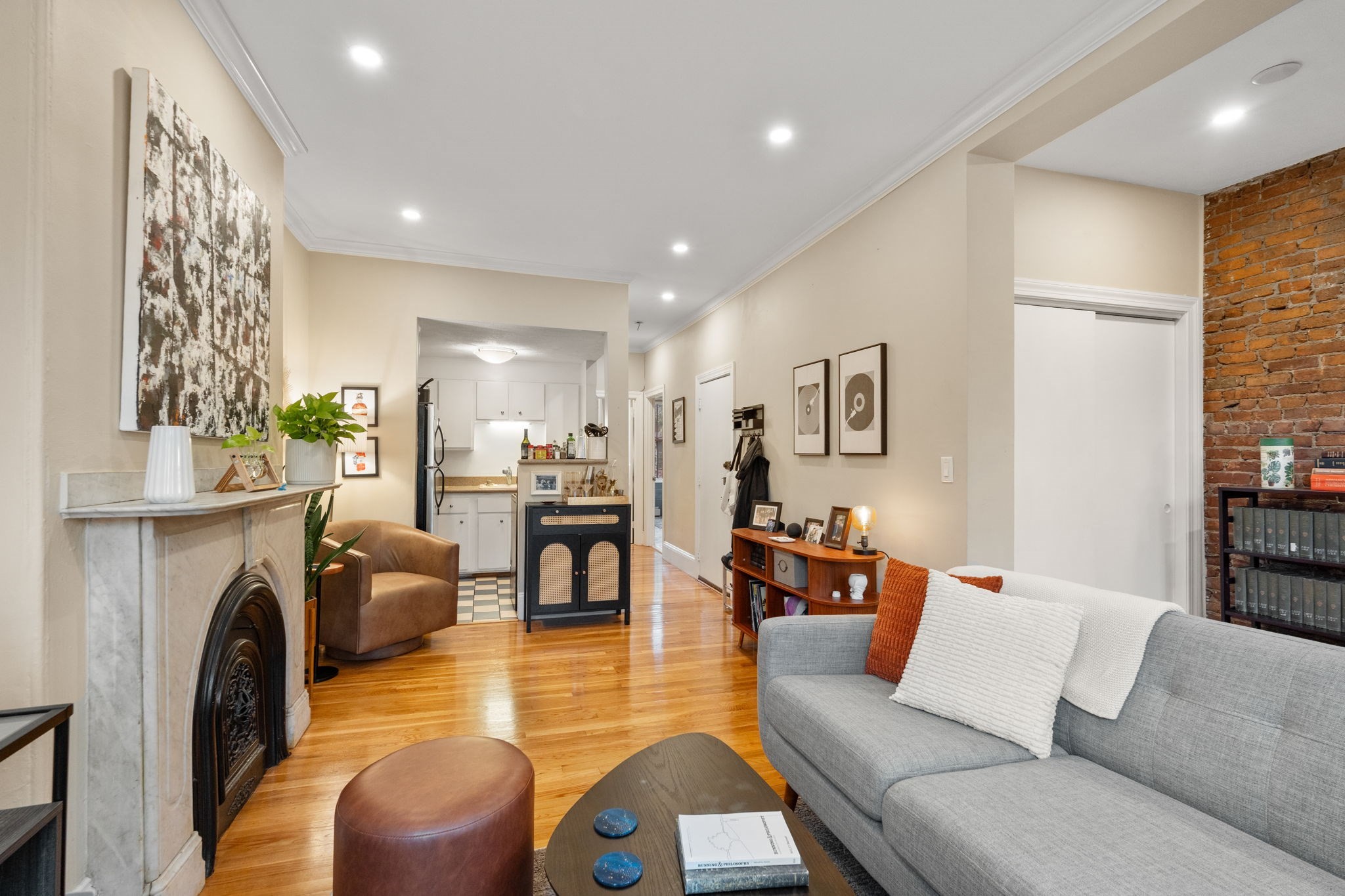 Living room with a marble fireplace, exposed brick wall, gray sofa, and open kitchen.