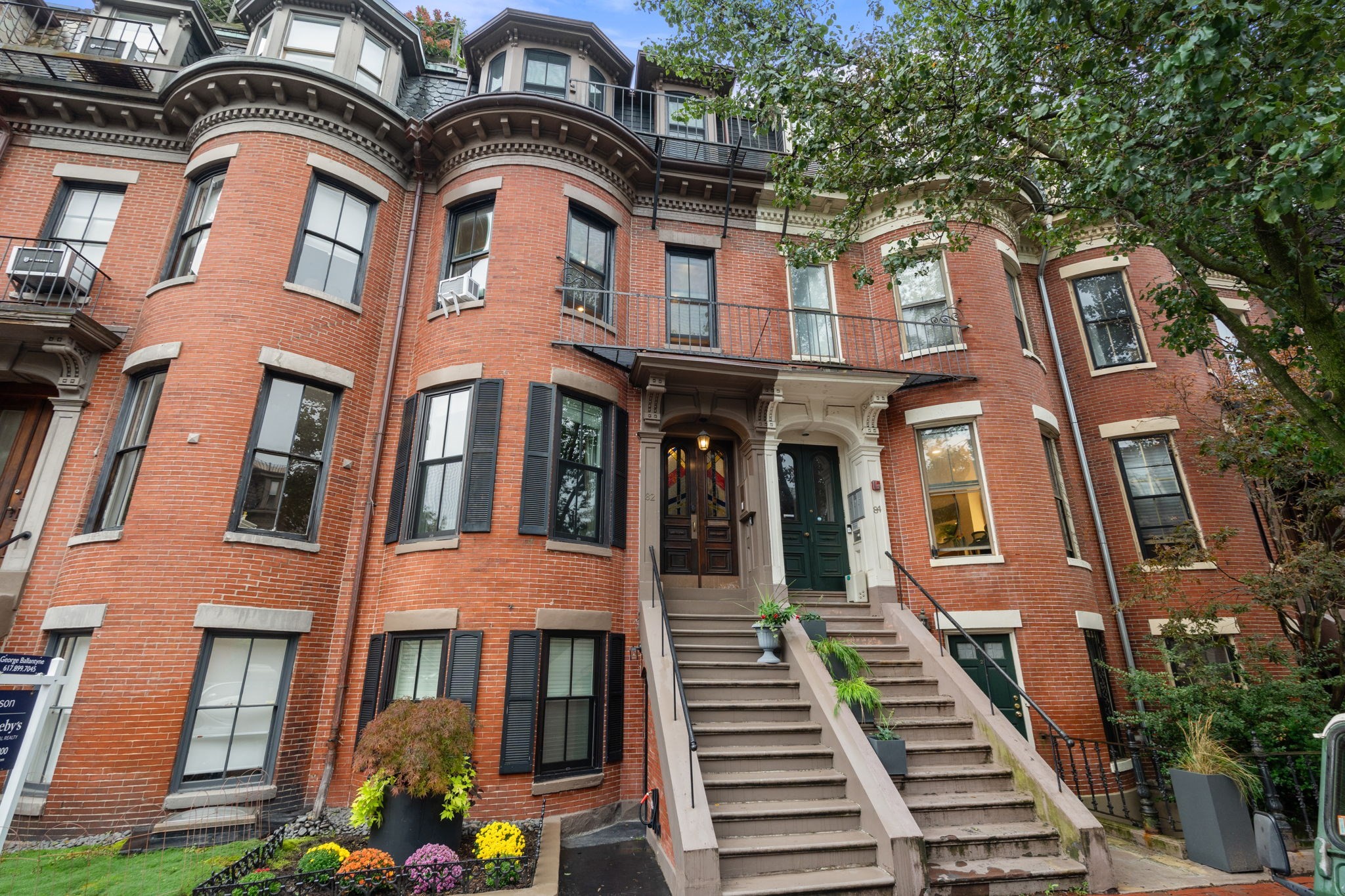 Red-brick residential building with bay windows, ornate trim, and raised entry stairways.