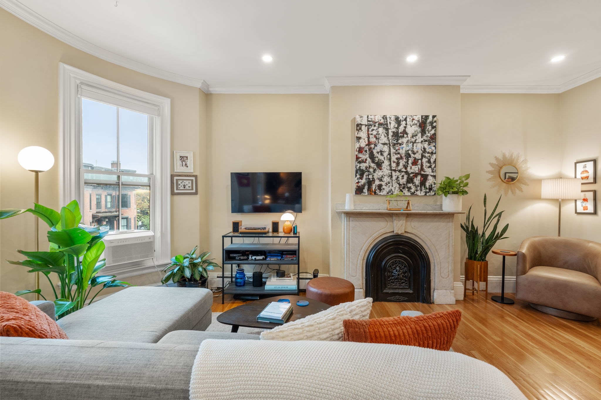 Living room with a marble fireplace, hardwood floors, and a gray sectional beside a large window.