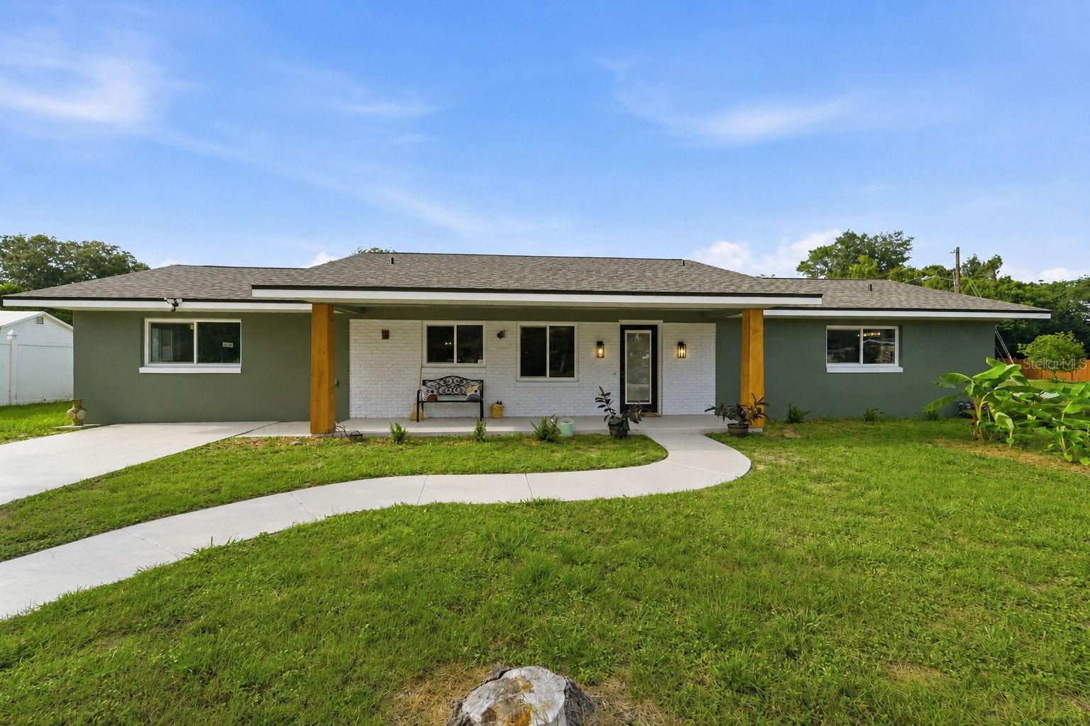 Single-story green home with a white brick porch and curved walkway across the front lawn.