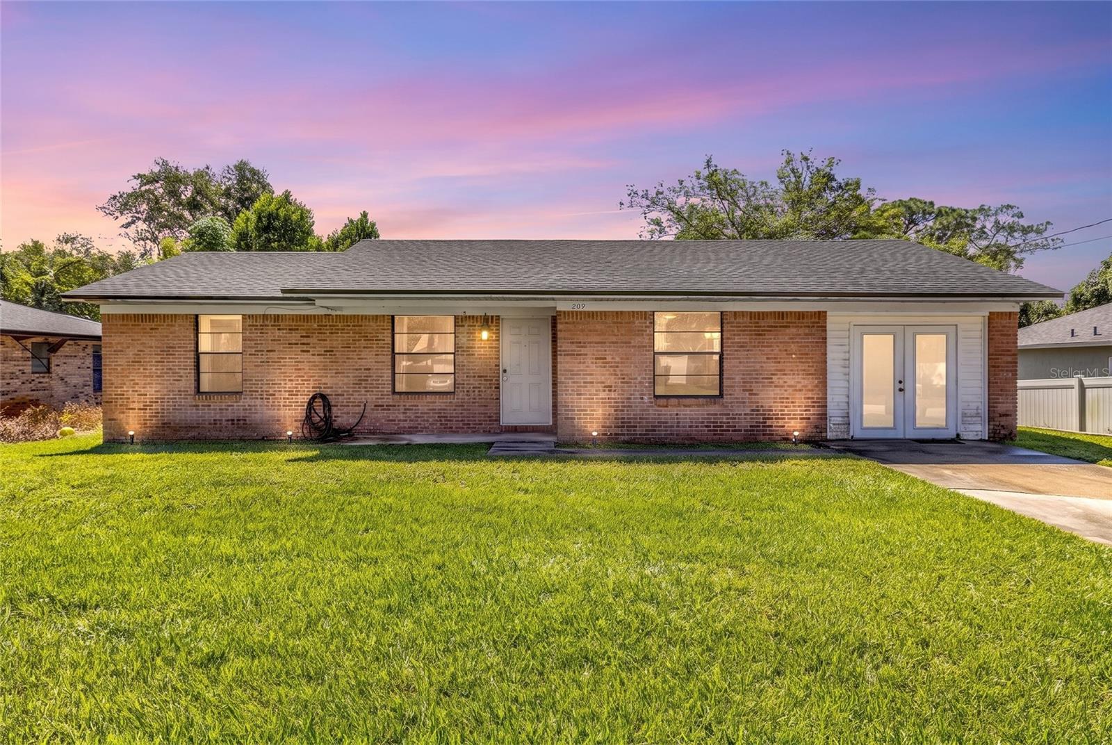 Single-story brick house with a broad lawn, white entry door, and pink-purple dusk sky.