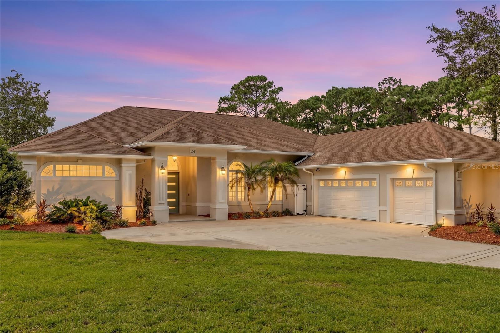 Single-story home with an illuminated entry, arched windows, and two garage doors at dusk.