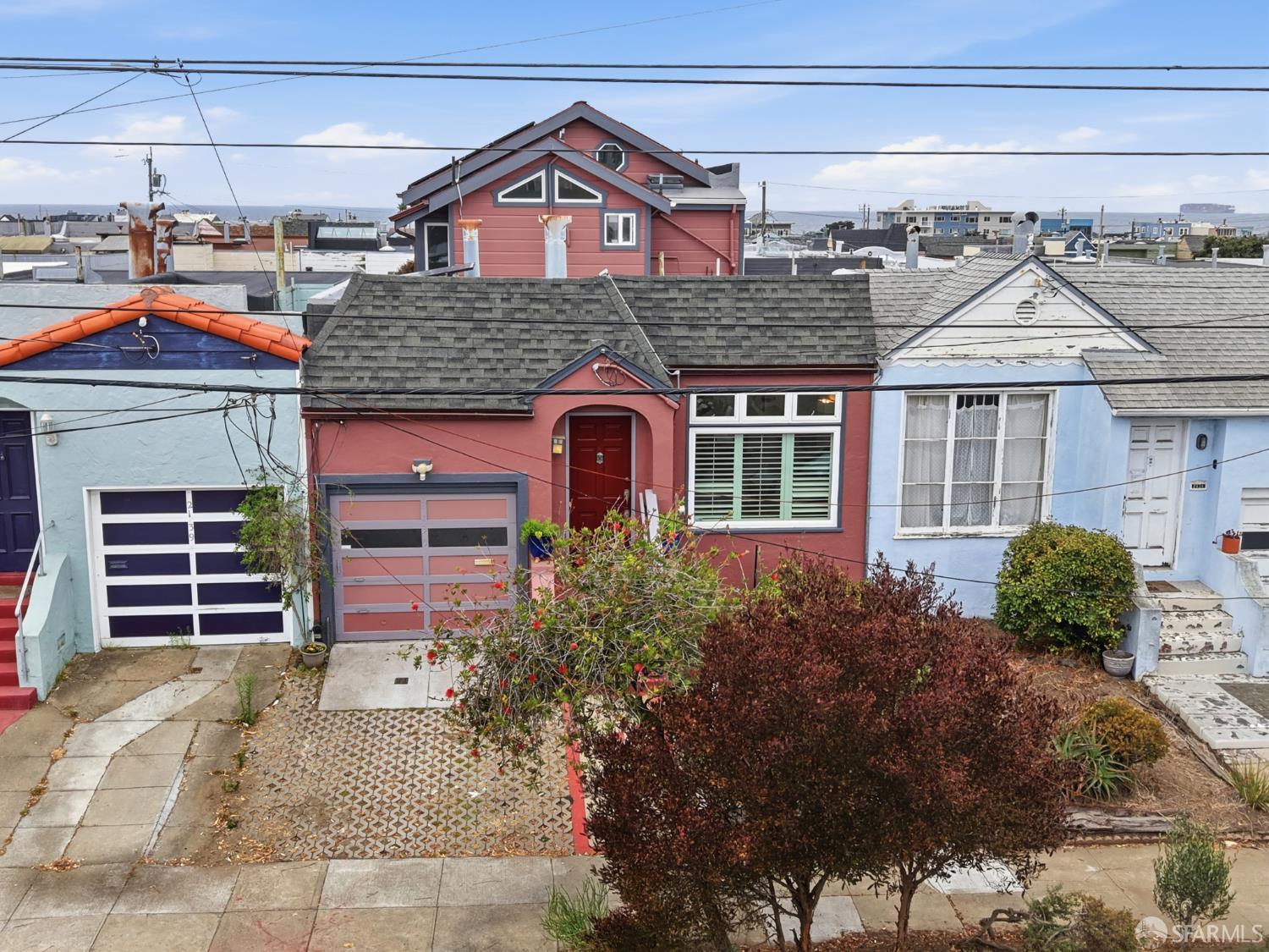 Red San Francisco home with a front garden, neighboring houses, and ocean visible in the distance.