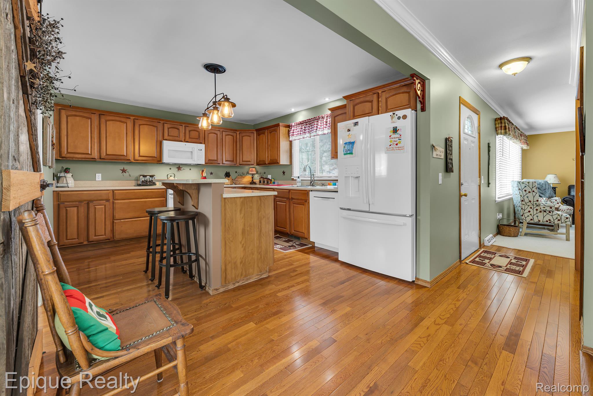 Kitchen with warm wood cabinets, hardwood floors, breakfast bar, and white appliances.