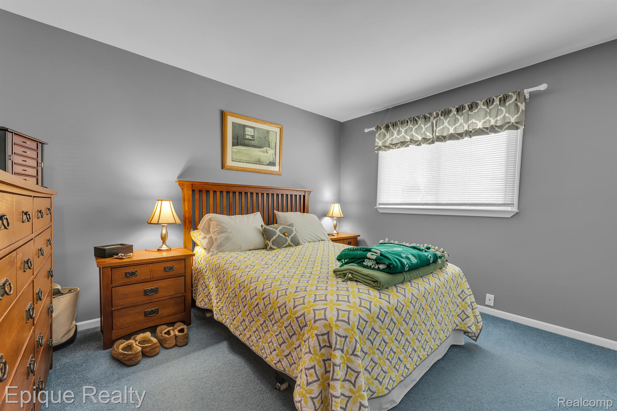 Furnished bedroom with a wooden bed, patterned yellow bedding, matching dressers, and gray walls.