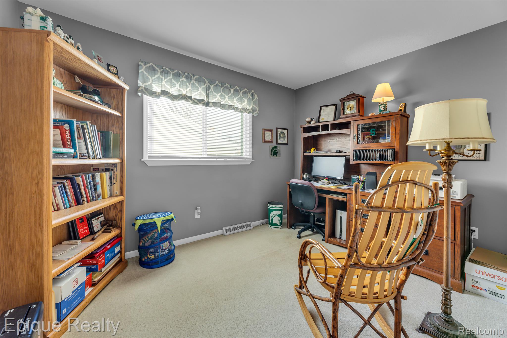Home office with a wooden bookcase, desk and hutch, and rocking chair by a large window.