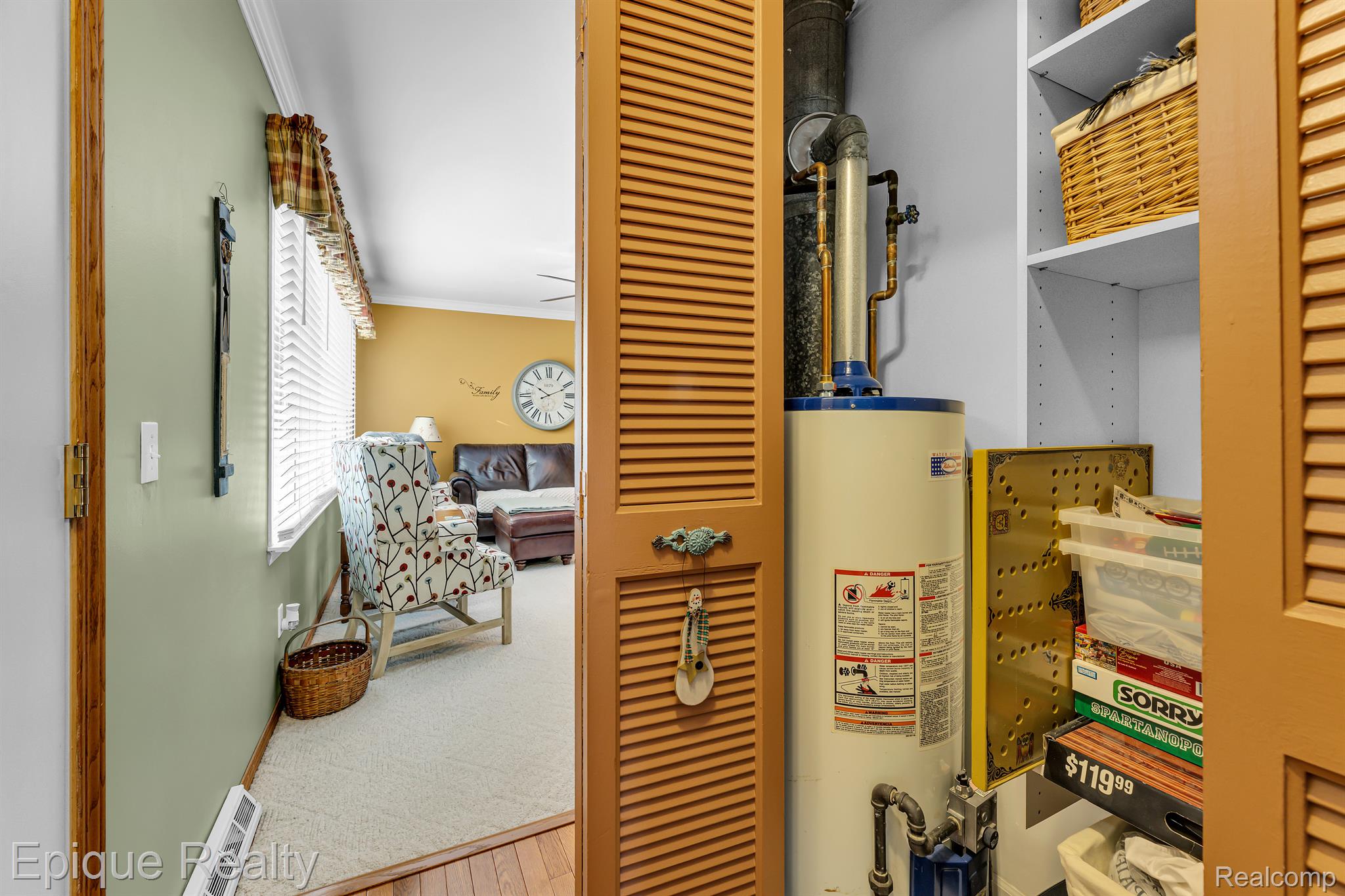 Utility closet with a large water heater and open louvered doors overlooking a furnished living room.