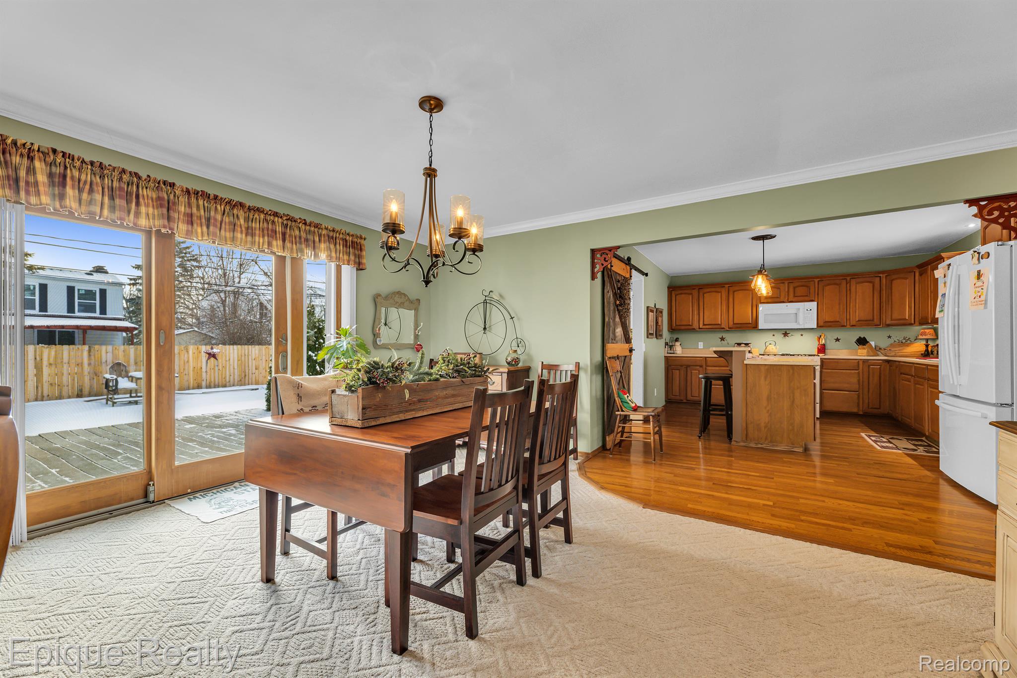 Dining room with a dark wood table beside glass doors, opening to a kitchen with warm wood cabinets.