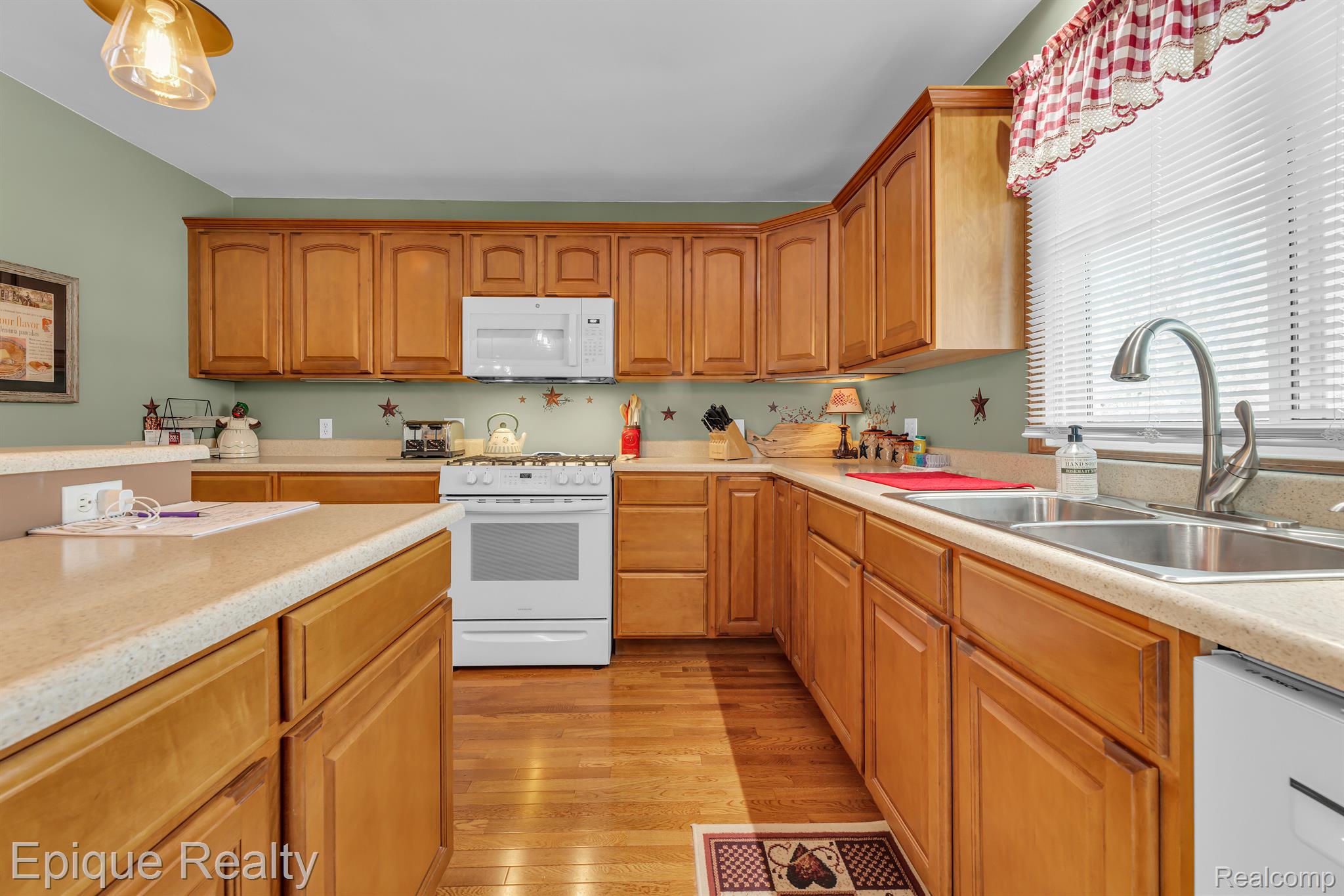 Kitchen with honey-colored cabinetry, hardwood floors, white appliances, and a double-basin sink.