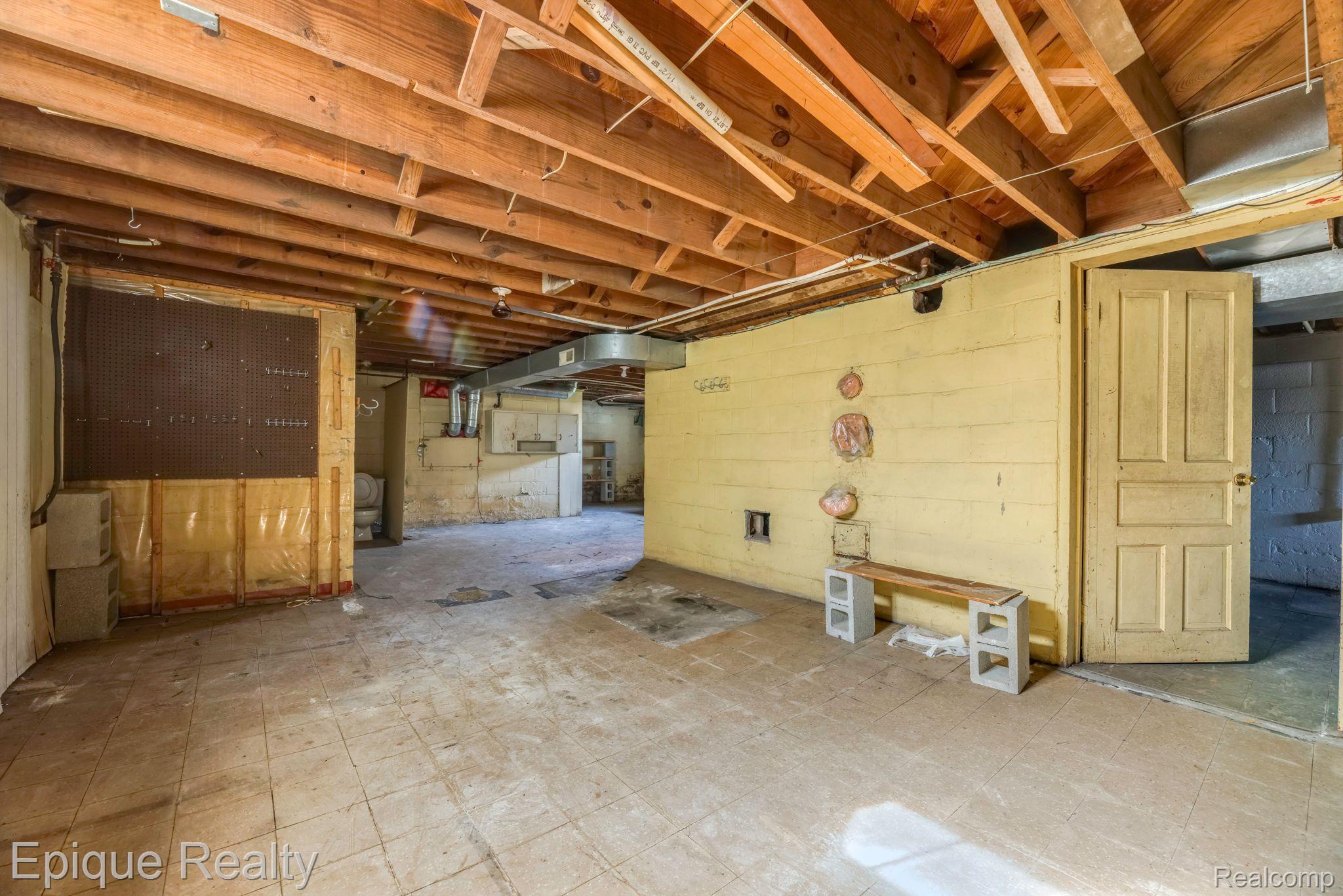 Unfinished basement with exposed ceiling joists, yellow masonry walls, and a simple workbench.