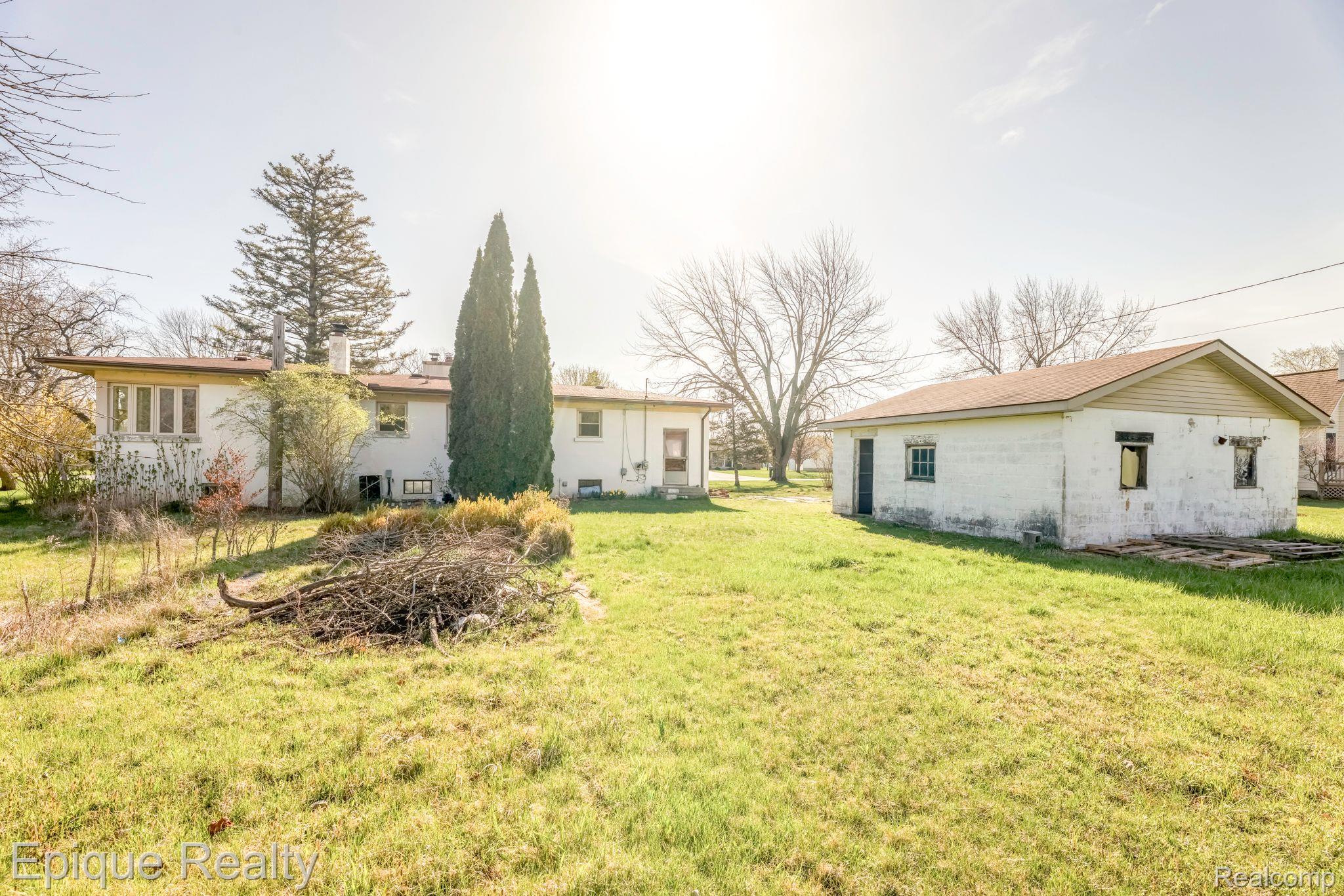 Rear of a house and separate white outbuilding across a grassy yard with a brush pile.
