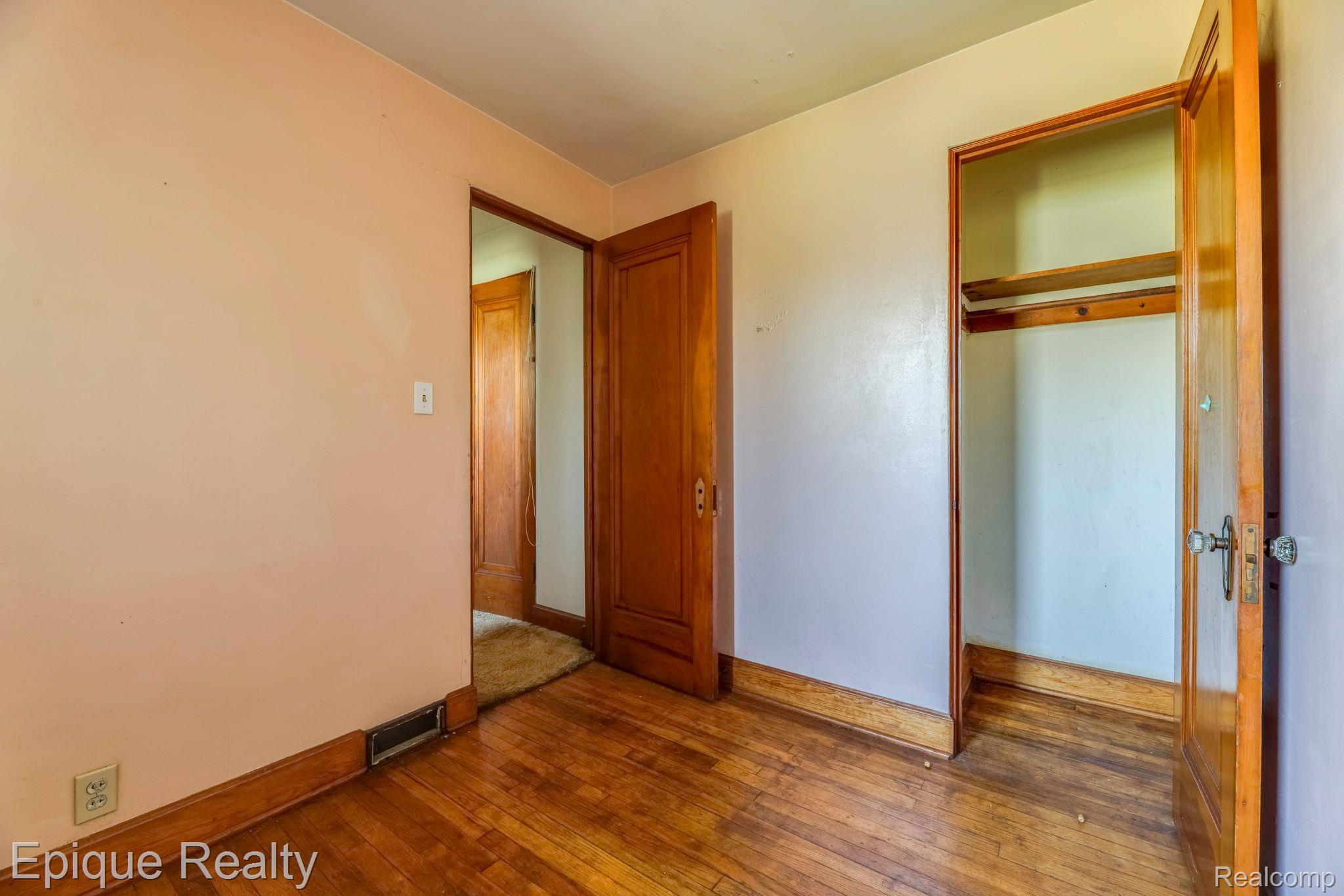 Empty bedroom with hardwood floors, wooden trim, and an open built-in closet.