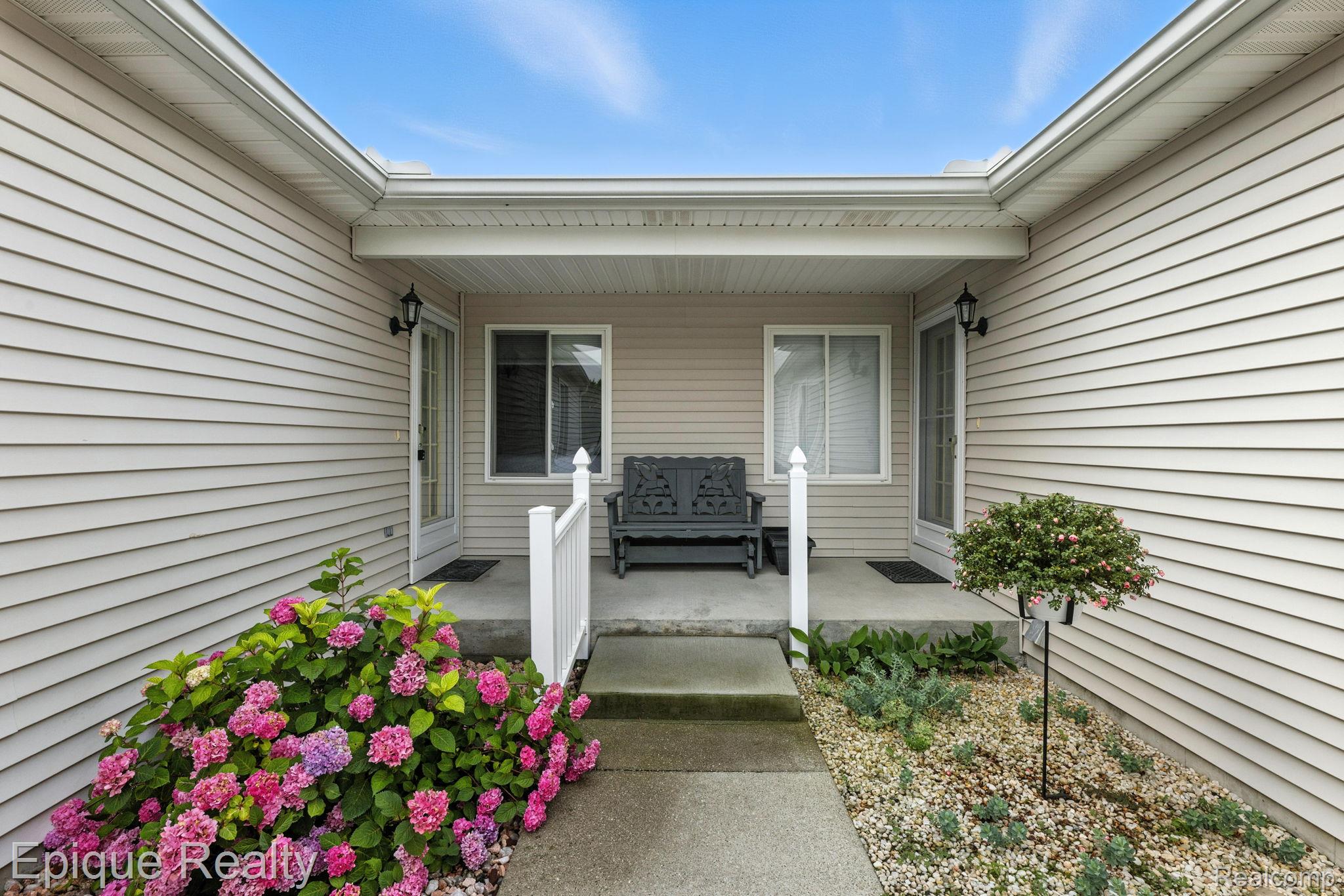 Covered porch with a black bench, concrete steps, and blooming hydrangeas.