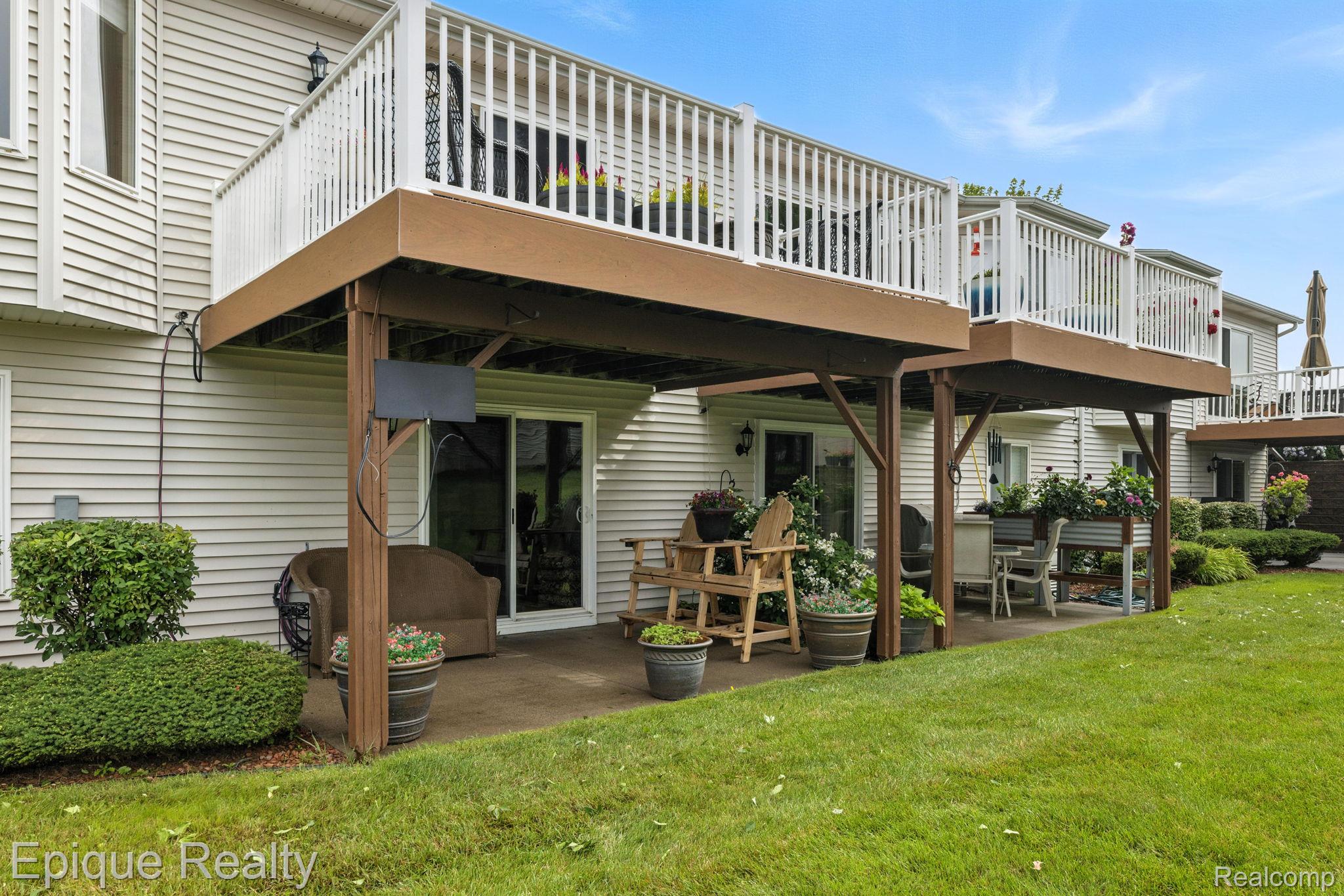 Home’s elevated deck overlooks a covered patio furnished with chairs, dining set, and flower planters.