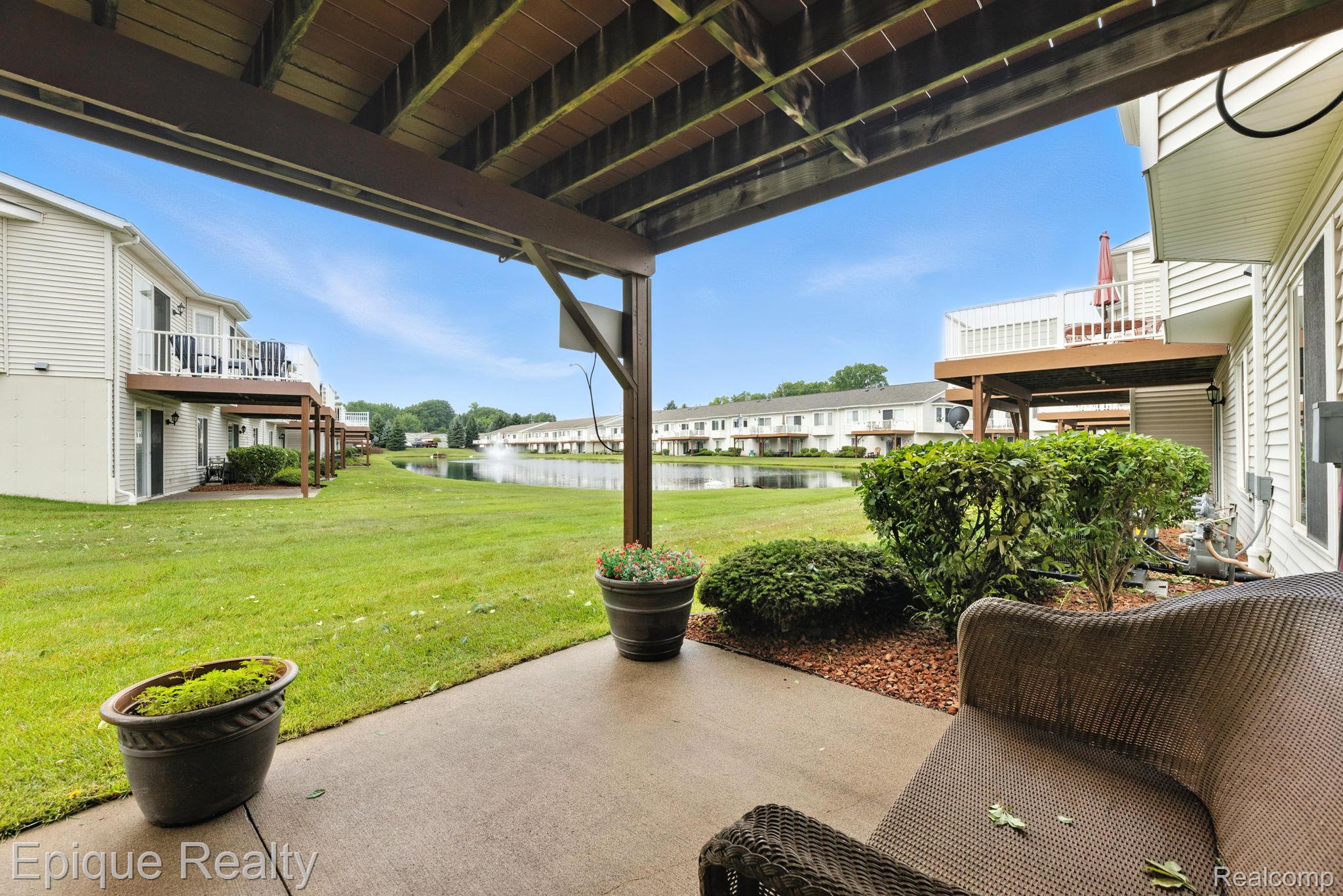 Covered patio overlooking a pond, with wicker seating, potted flowers, and neighboring townhomes.