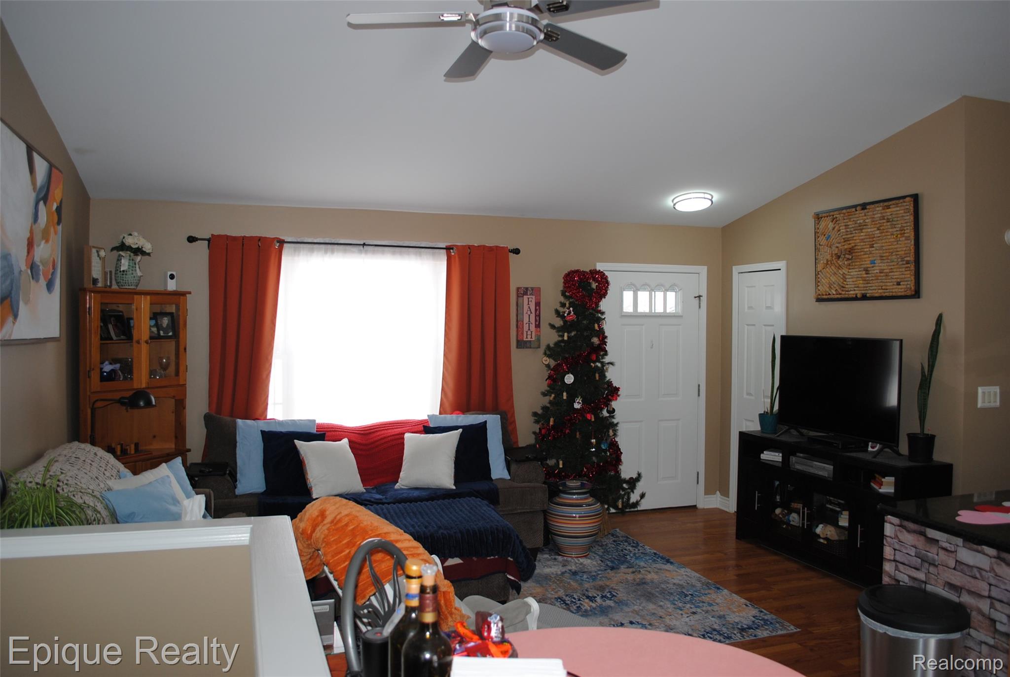 Living room with red curtains, a decorated Christmas tree, and a television above a fireplace.