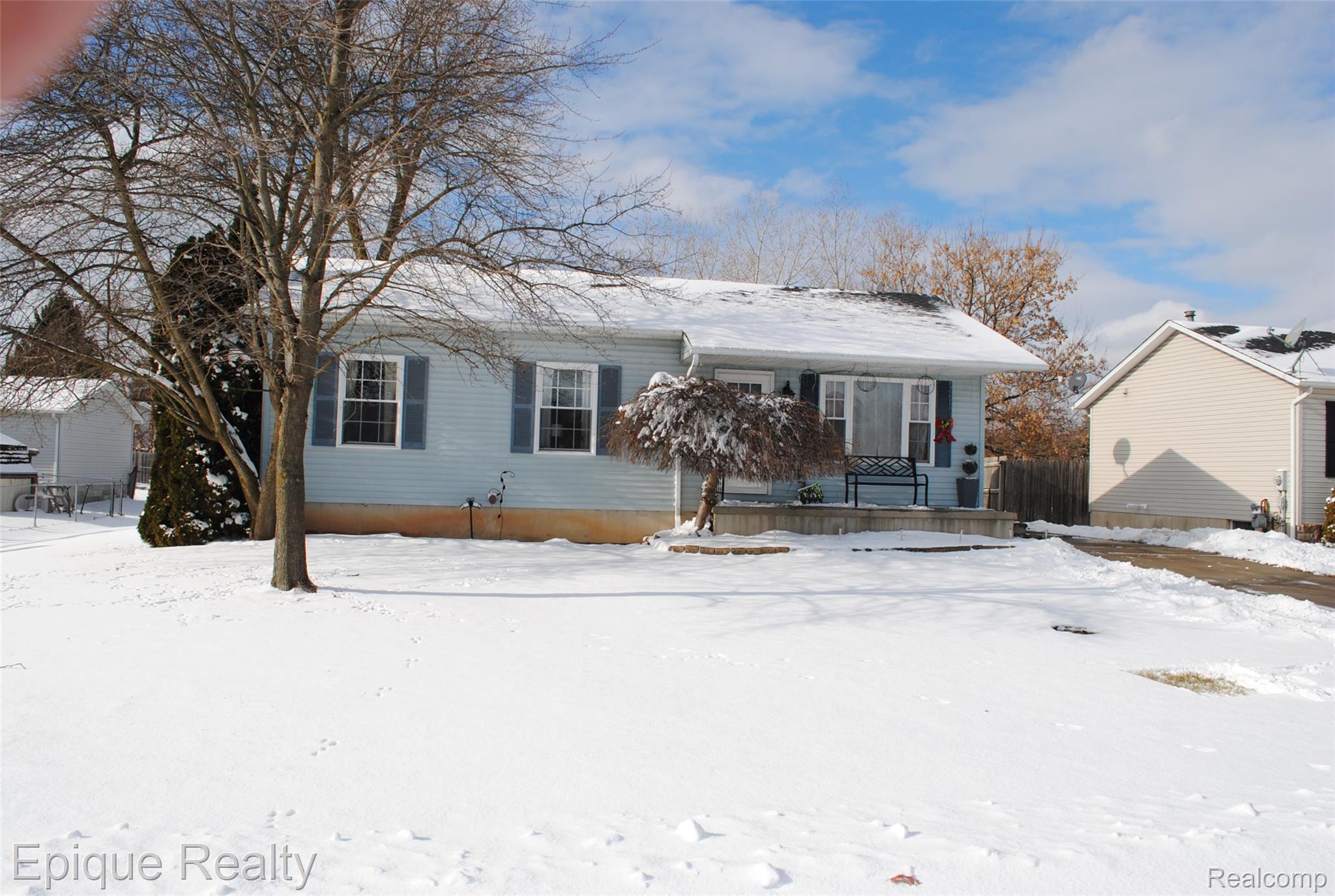Single-story blue house with shutters and a small entry deck, viewed across a snow-covered yard.